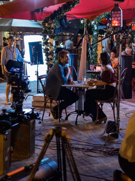 Crew members with equipment in front of man and woman sitting at a table in a restaurant