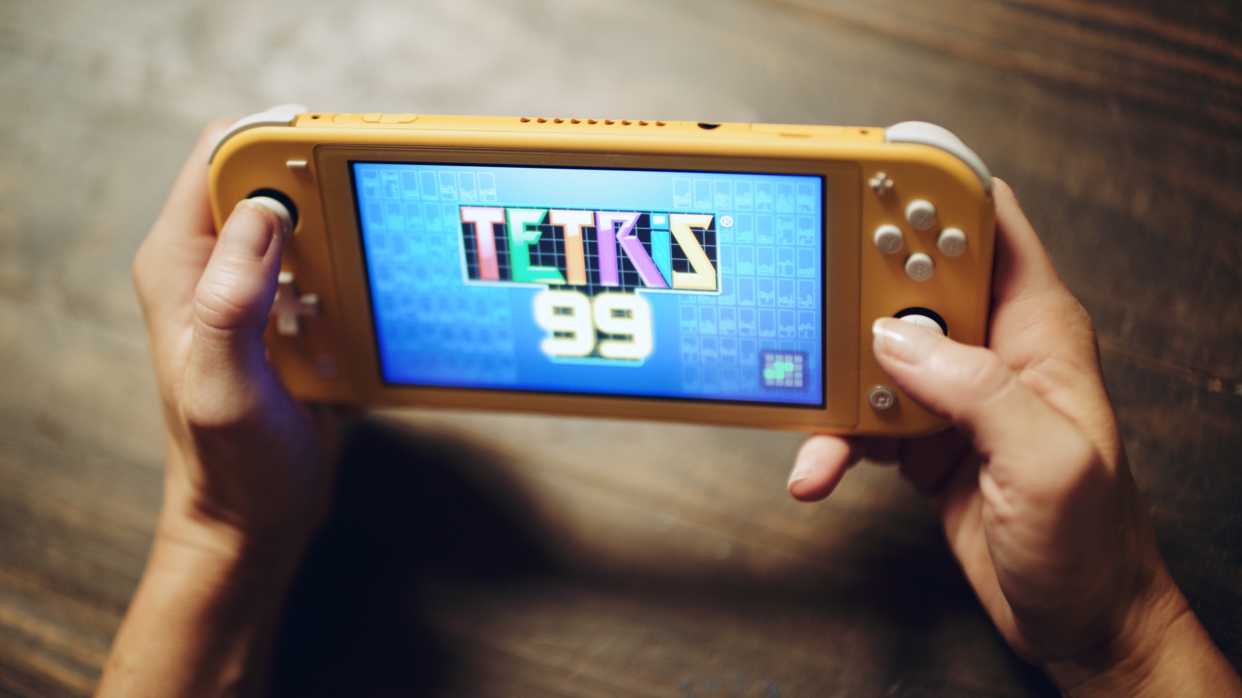 Reach Out and Play Social Closeup of hands holding a video game console with Tetris 99 game title screen loading