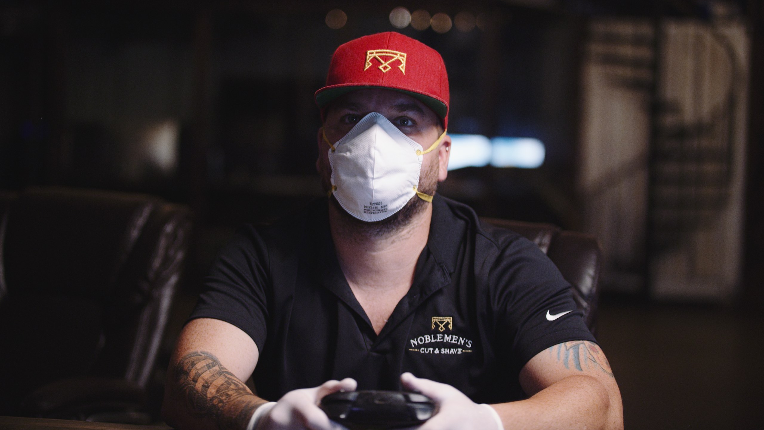 IU C&I Studios Portfolio Reach Out and Play Tattooed man wearing red cap, black shirt and white mask using video game controller wearing white latex gloves