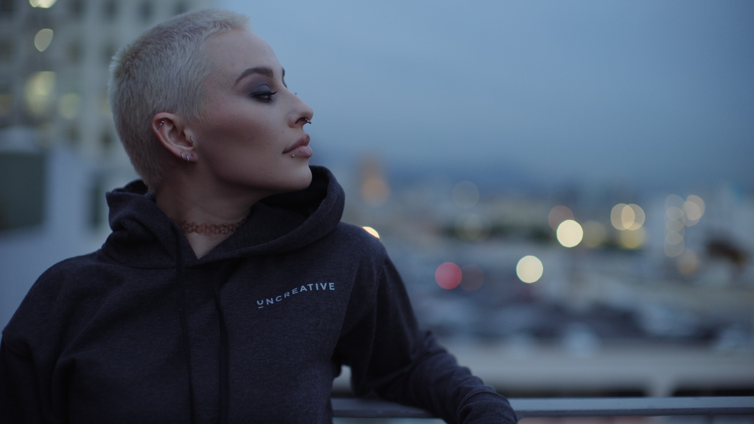 Uncreative Shop LA Apparel on available at the Uncreative Shop Woman with short blond hair wearing nose rings, jewelry and gray hoodie looking off to the side over her shoulder
