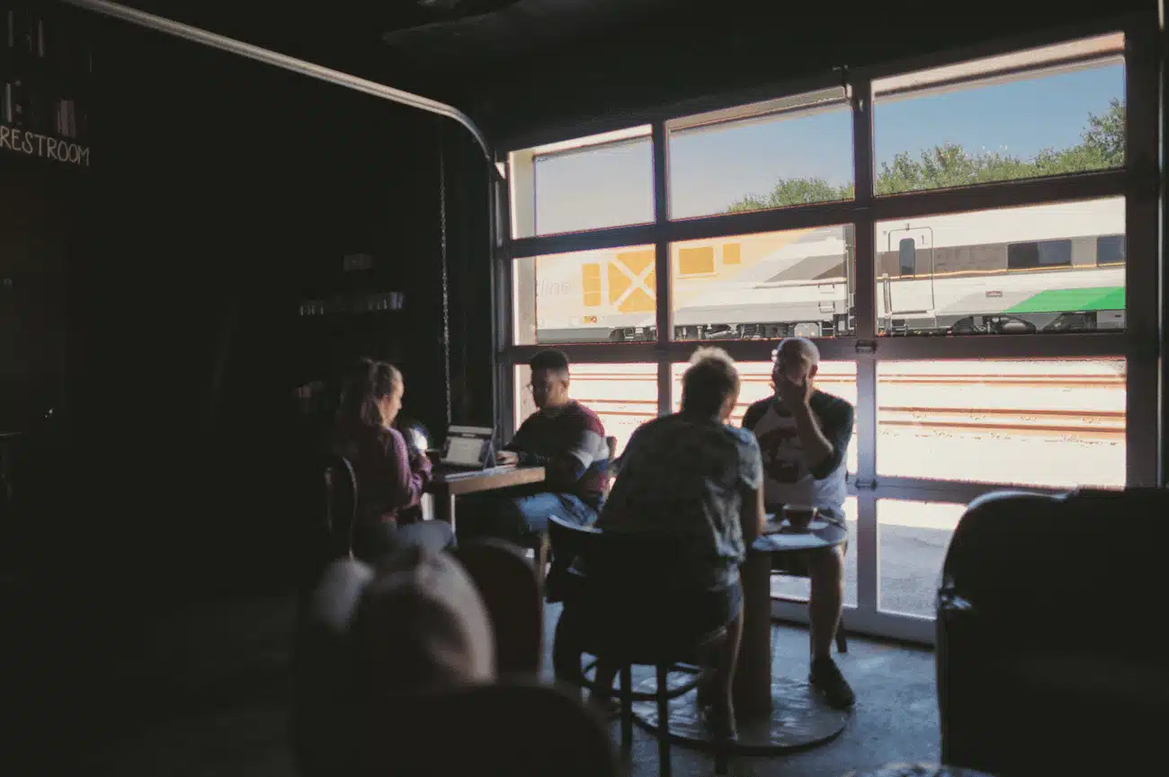 People sitting by window in a building with train and tracks in the background outside