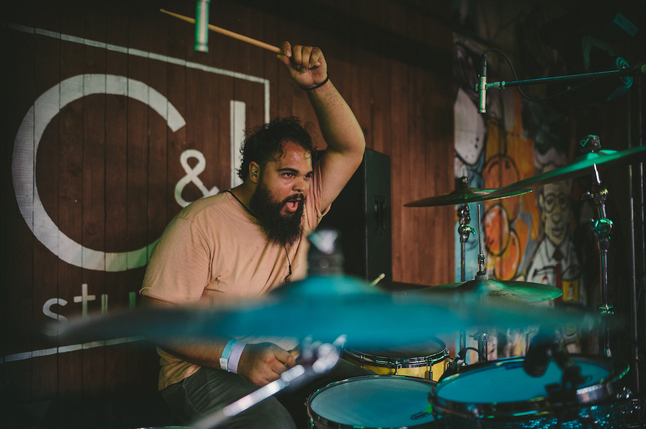 LP Man with bushy beard wearing a peach colored shirt playing drums