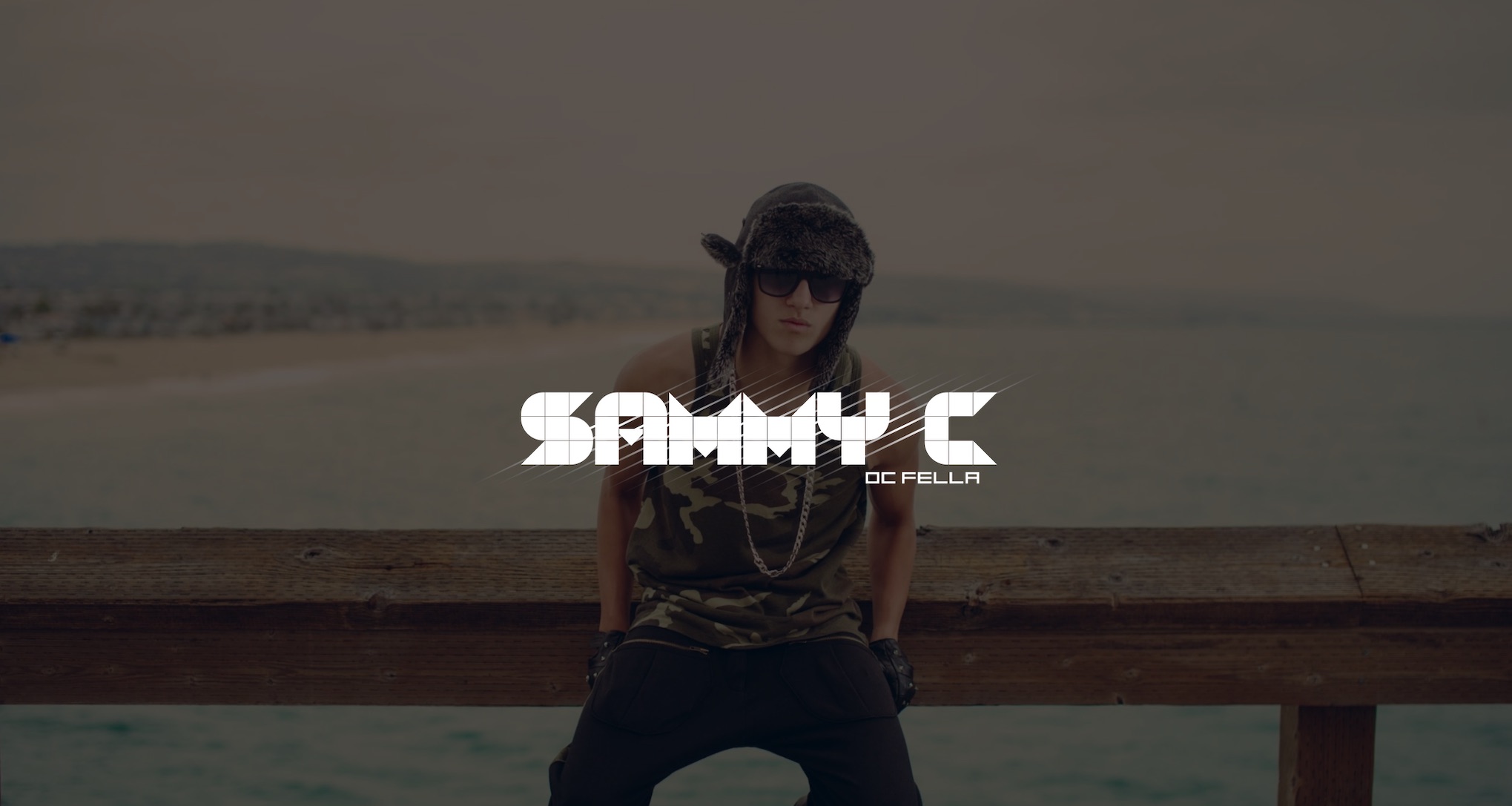 Keyword: Artist Management Services .SammyC Artist Management Services White SammyC DC Fella logo on dimmed background of young man wearing a winter hat and camouflage tank top with chain, leather gloves and black pants