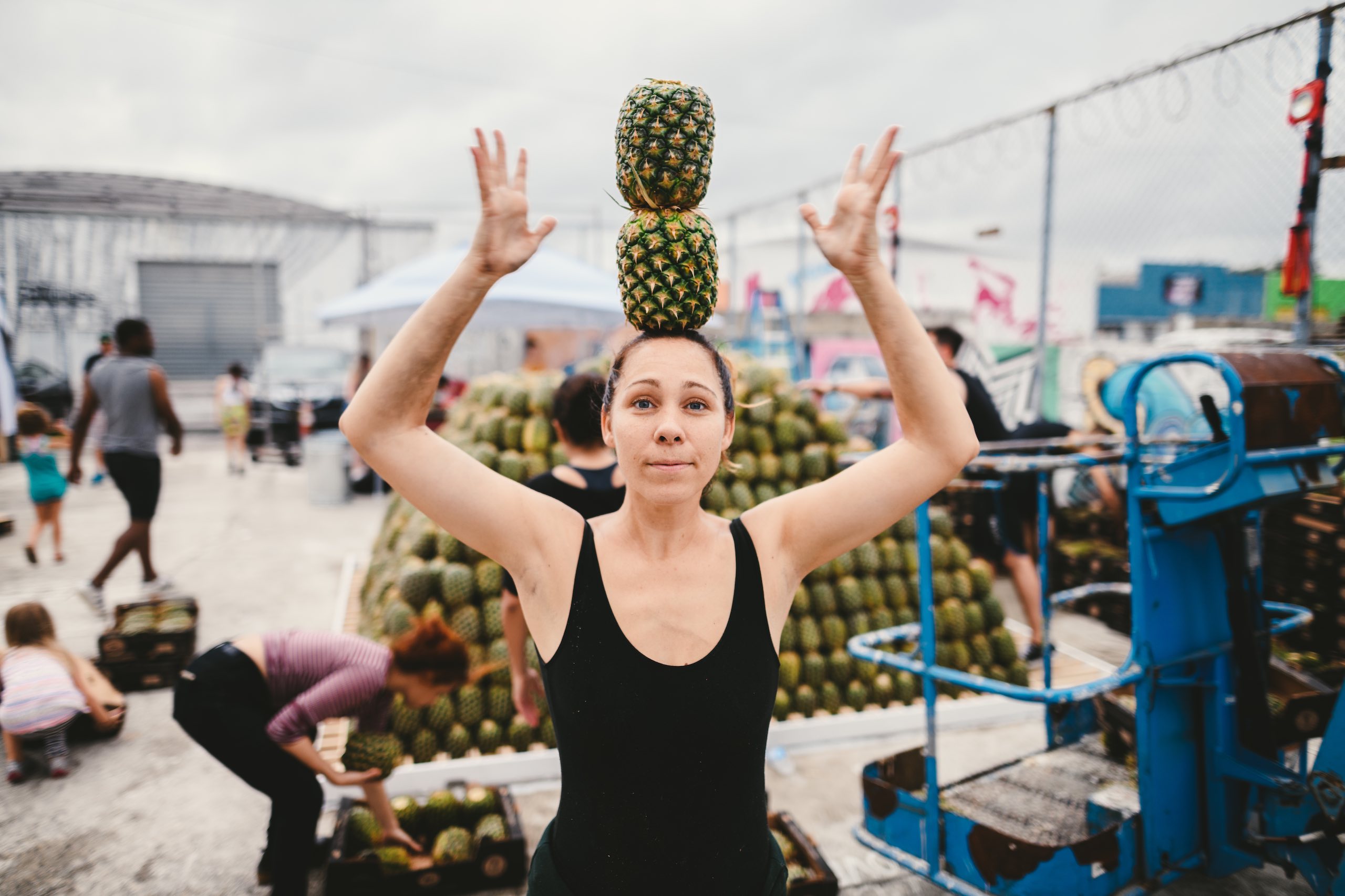 Artwalk 2018 May Pineapple Pyramid Woman wearing black tank top balancing two pineapples on her head with pineapple pyramid in the background