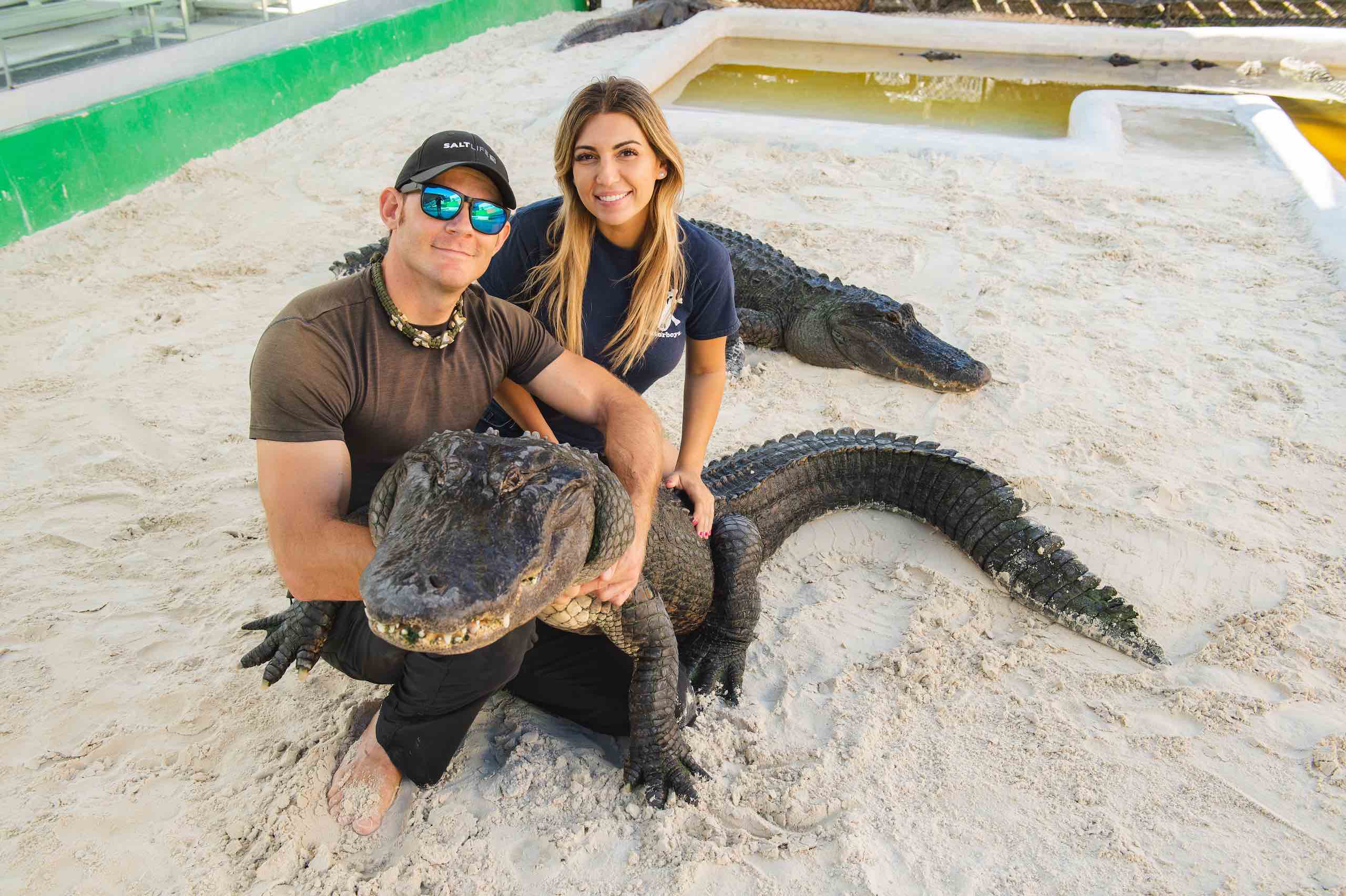 Everglades Holiday Park Muscular man and woman posing with alligators in a sand pit