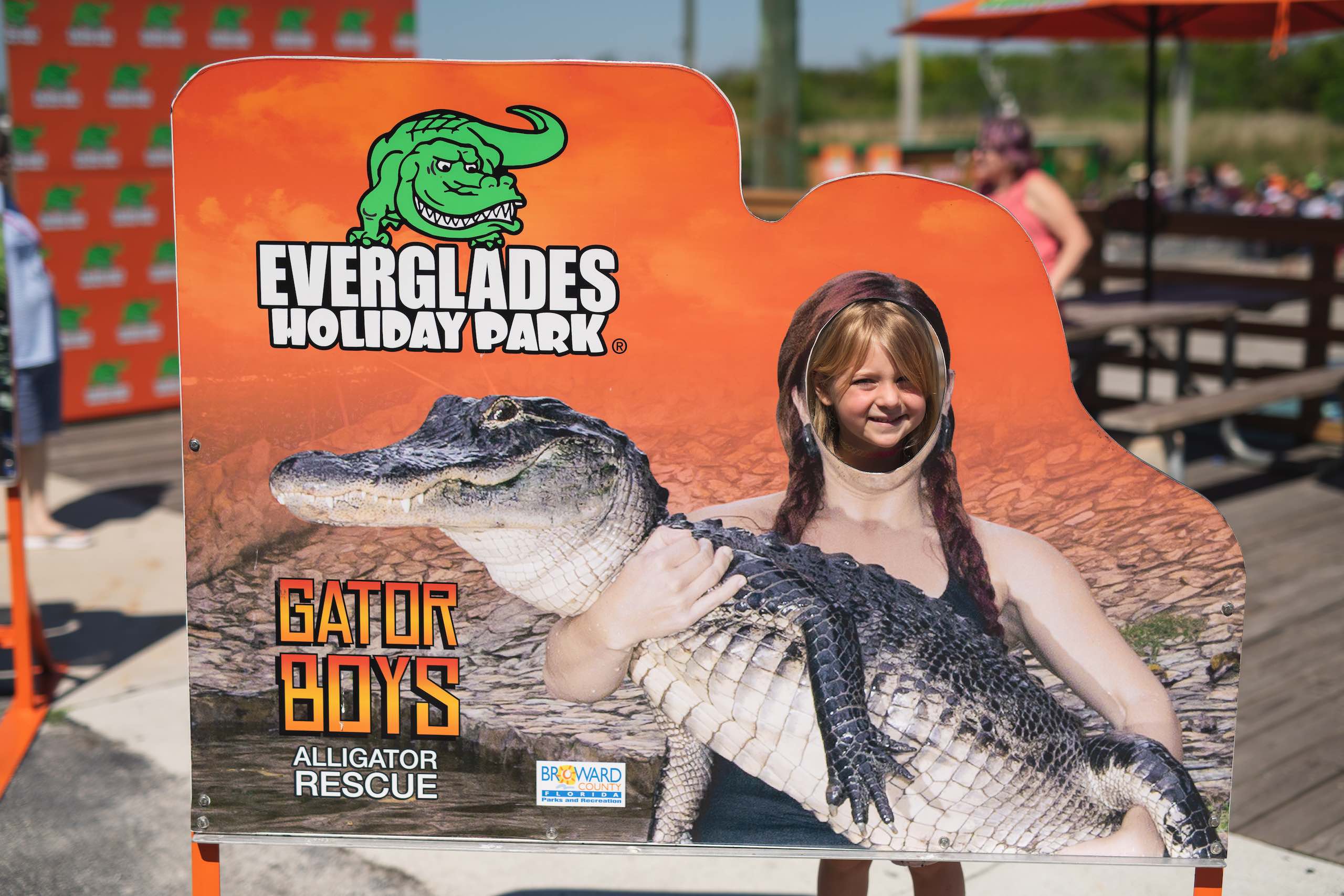 Everglades Holiday Park Closeup of girl looking through hole of a cutout of someone holding an alligator in her arms