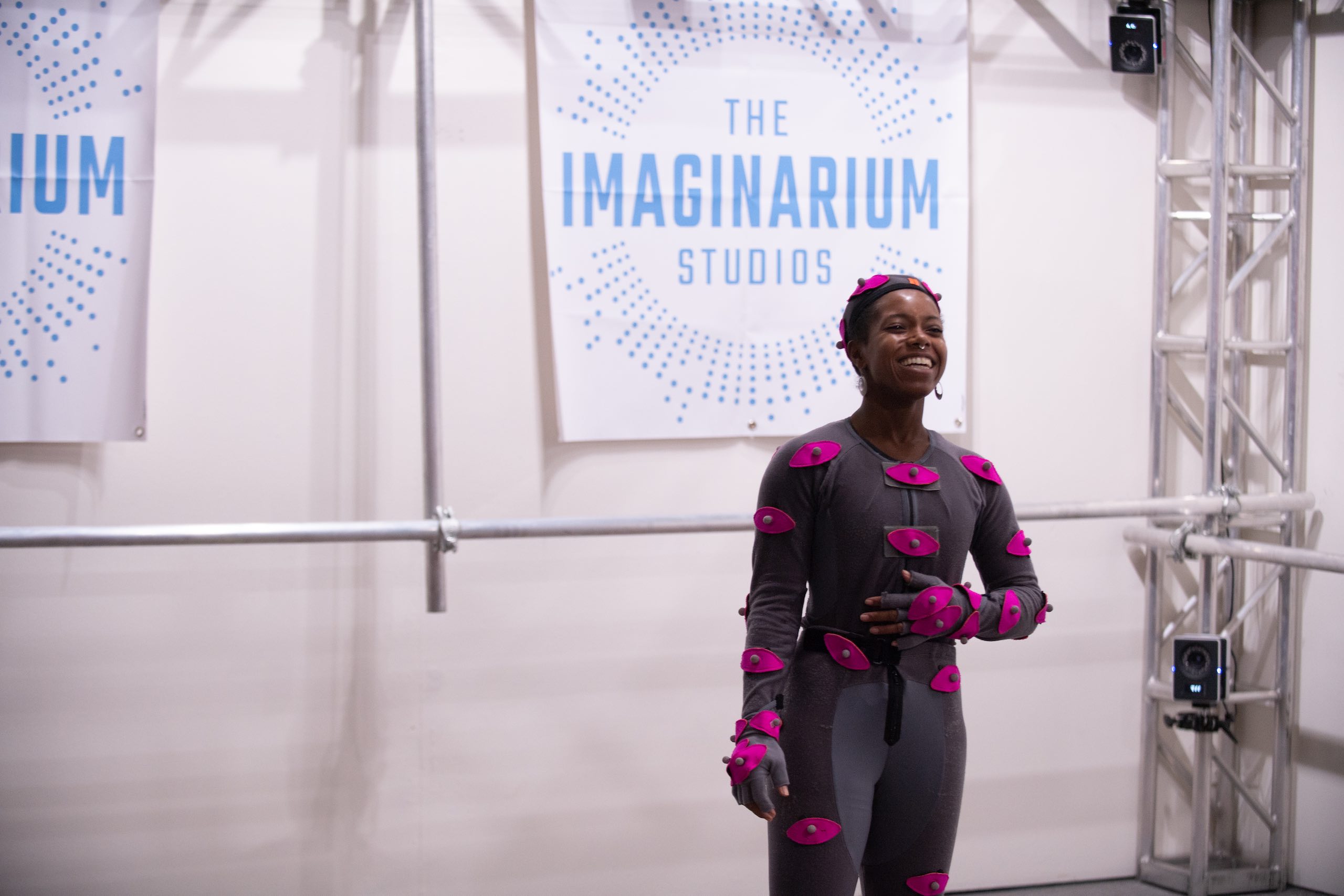 Woman with pink body movement sensors smiling in front of The Imaginarium Studios sign