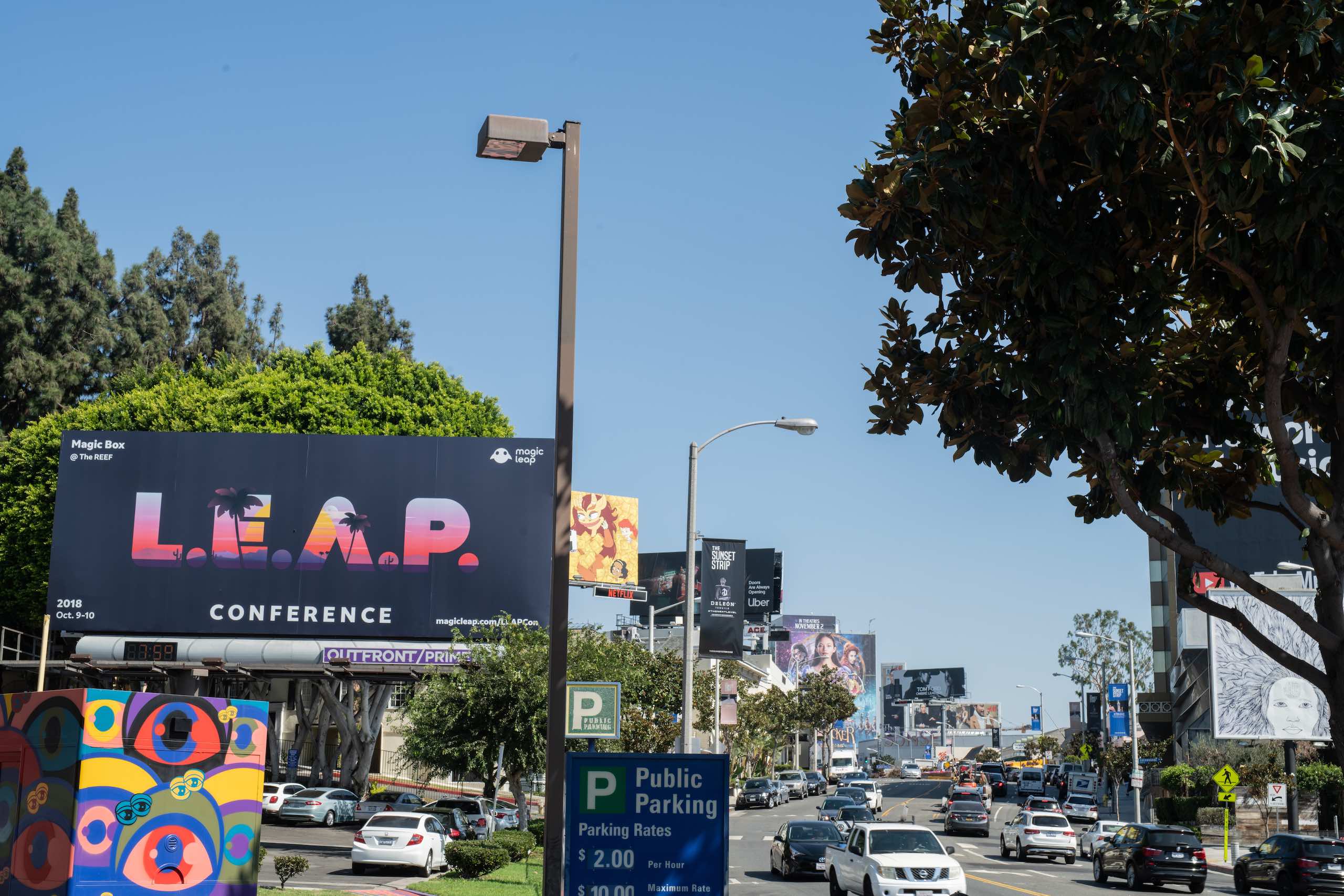 LEAP Conference billboard on display by a parking lot in city near road with cars parked and driving by