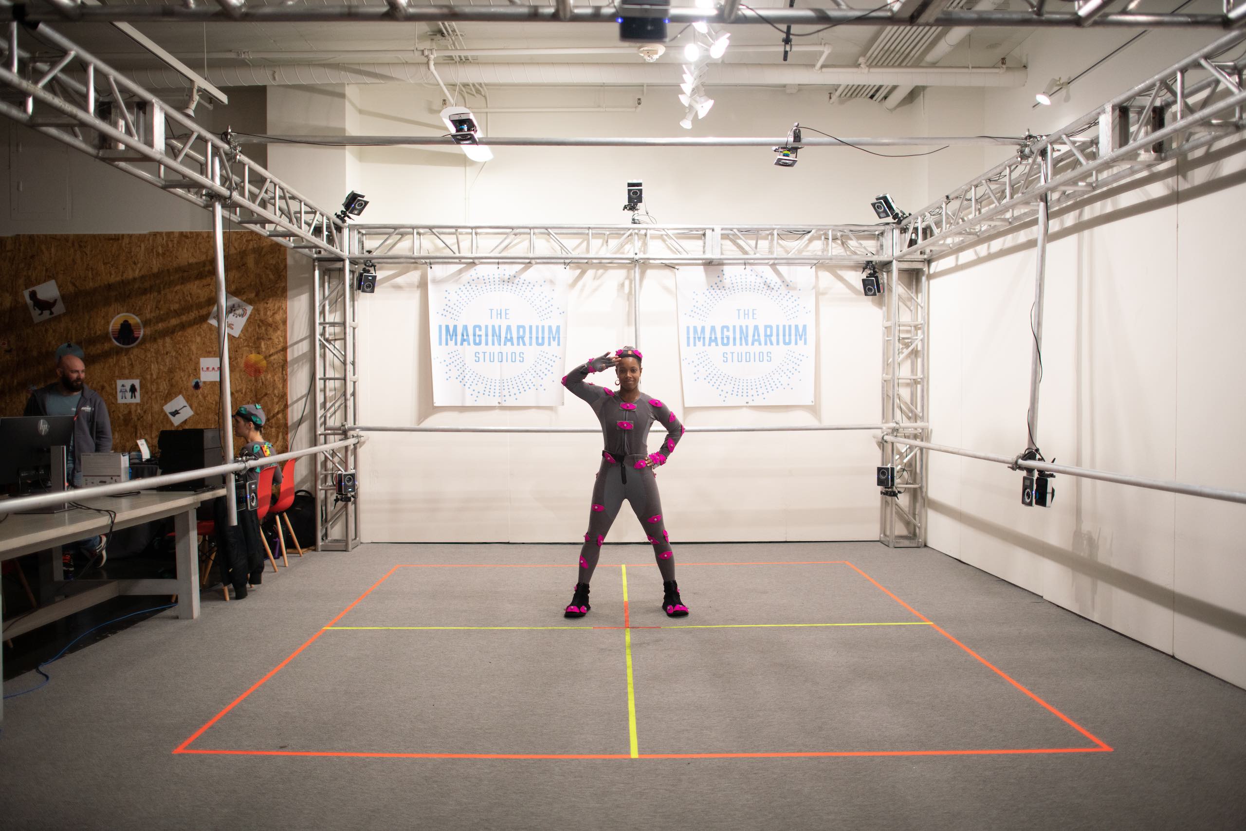 Woman with pink body movement sensors smiling and posing doing a salute in front of The Imaginarium Studios signs