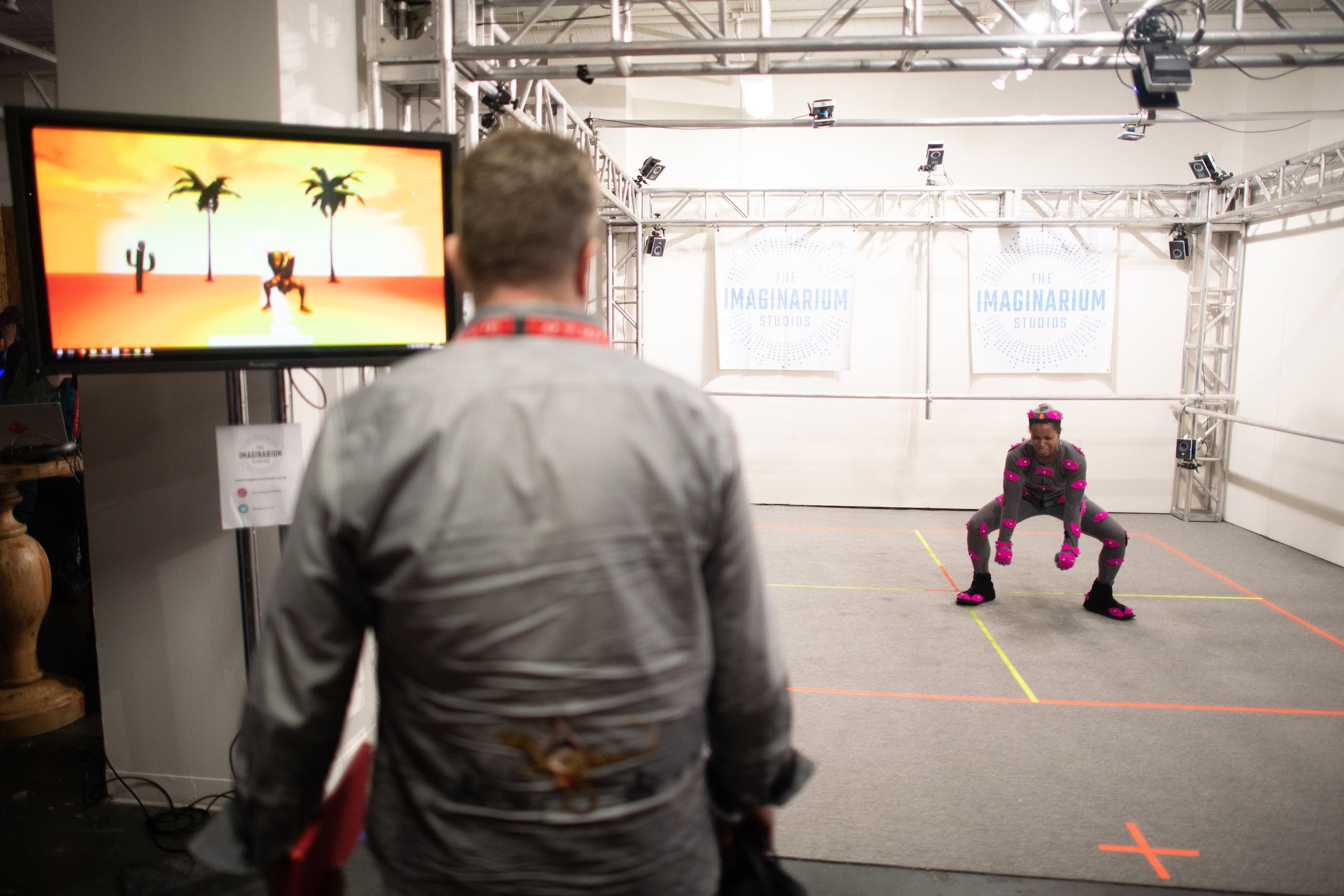 Woman with pink body movement sensors doing moves while man views a monitor with character mimicking her moves in The Imaginarium Studios