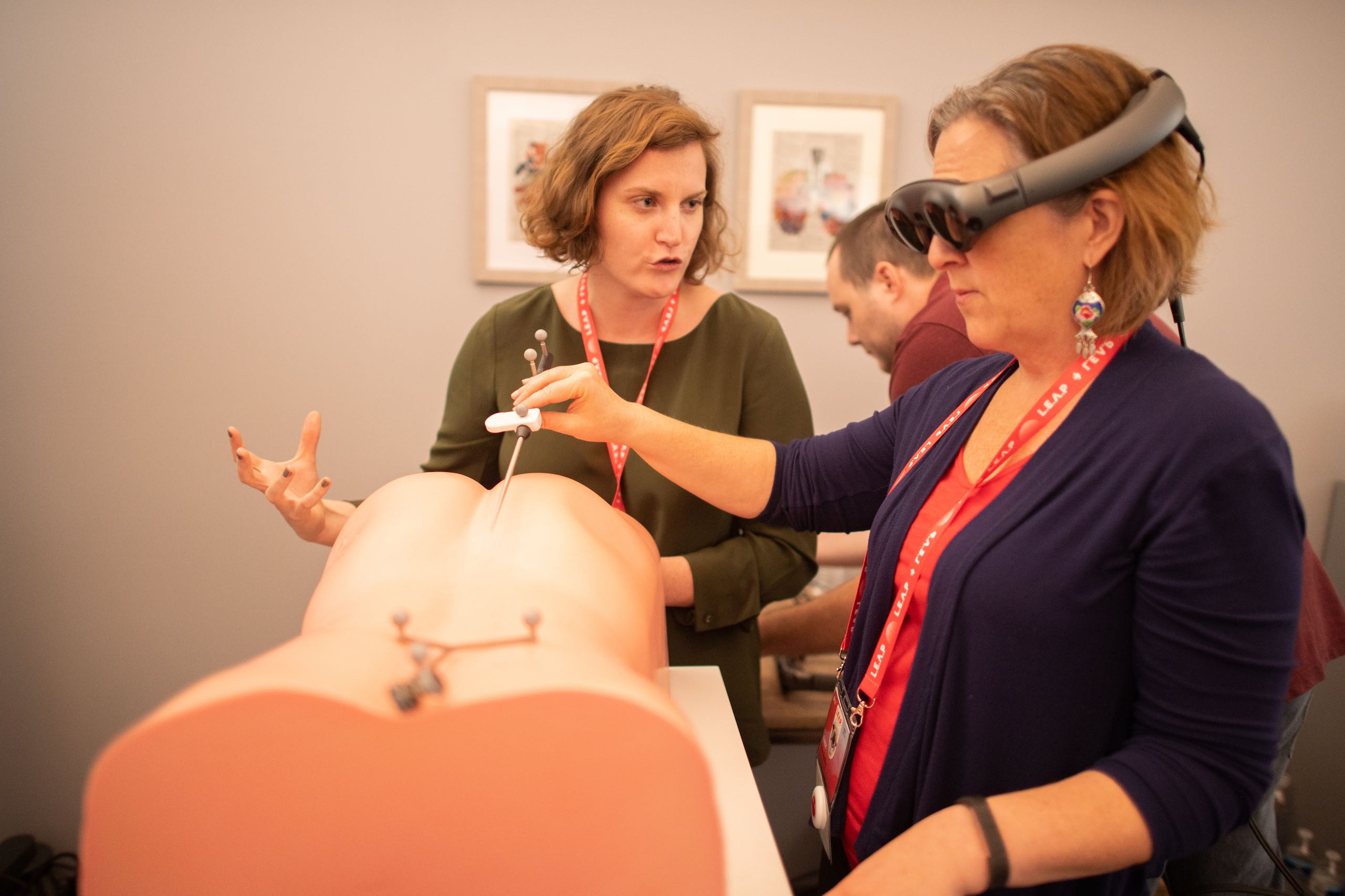 Side profile of a woman wearing Lightwear equipment using a probe in a medical dummy being instructed by another woman