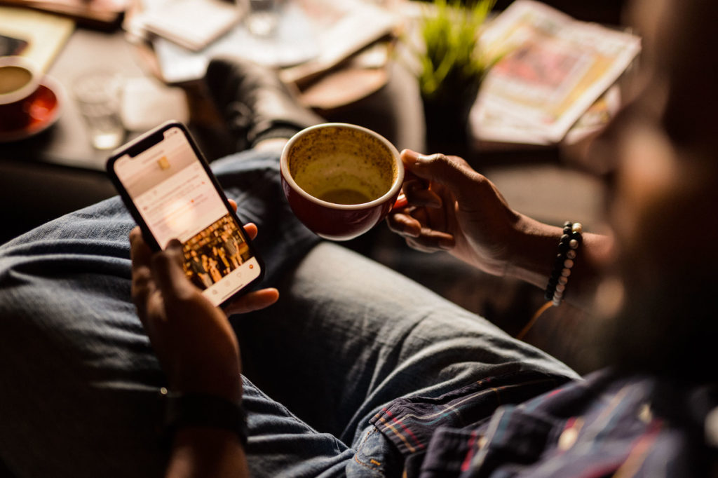 Brew Social Media View from over the shoulder of a man wearing jeans looking at his cellphone holding a small red cup