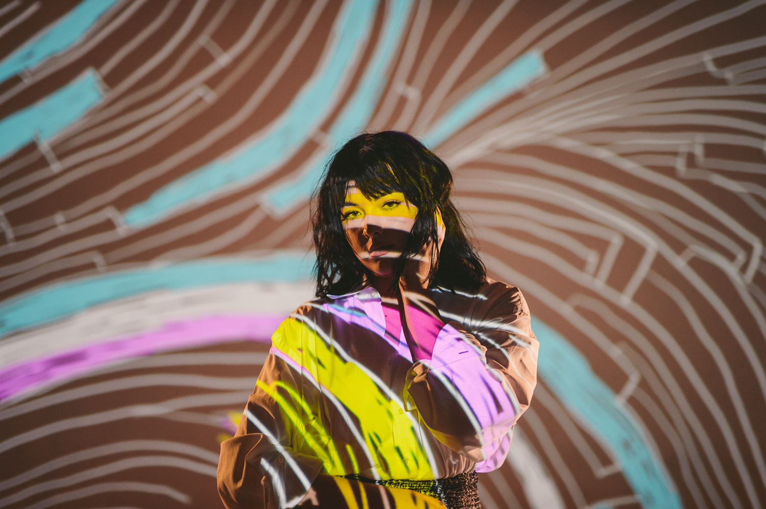 Artwalk Self Projection with woman with black hair posing for camera with multiple colored artwork being projected on her
