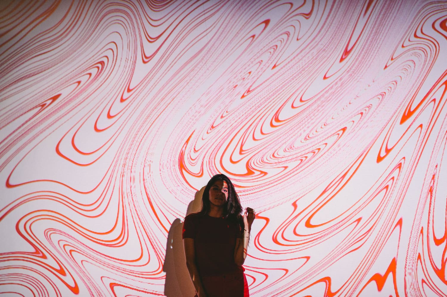 Woman with long brown hair posing for camera with red and white colored artwork being projected on her