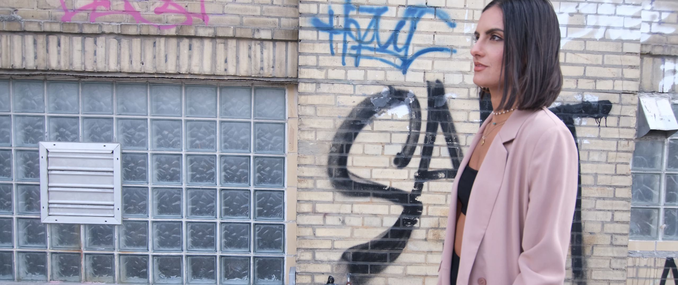 Uncreative Radio with Hana Ostapchuk with a side profile of her wearing a pink dress jacket on a street with graffiti behind her
