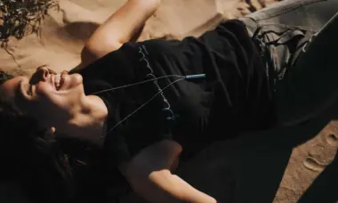 View from above of woman laying in the sand wearing black top, jeans and a whistle around her neck smiling