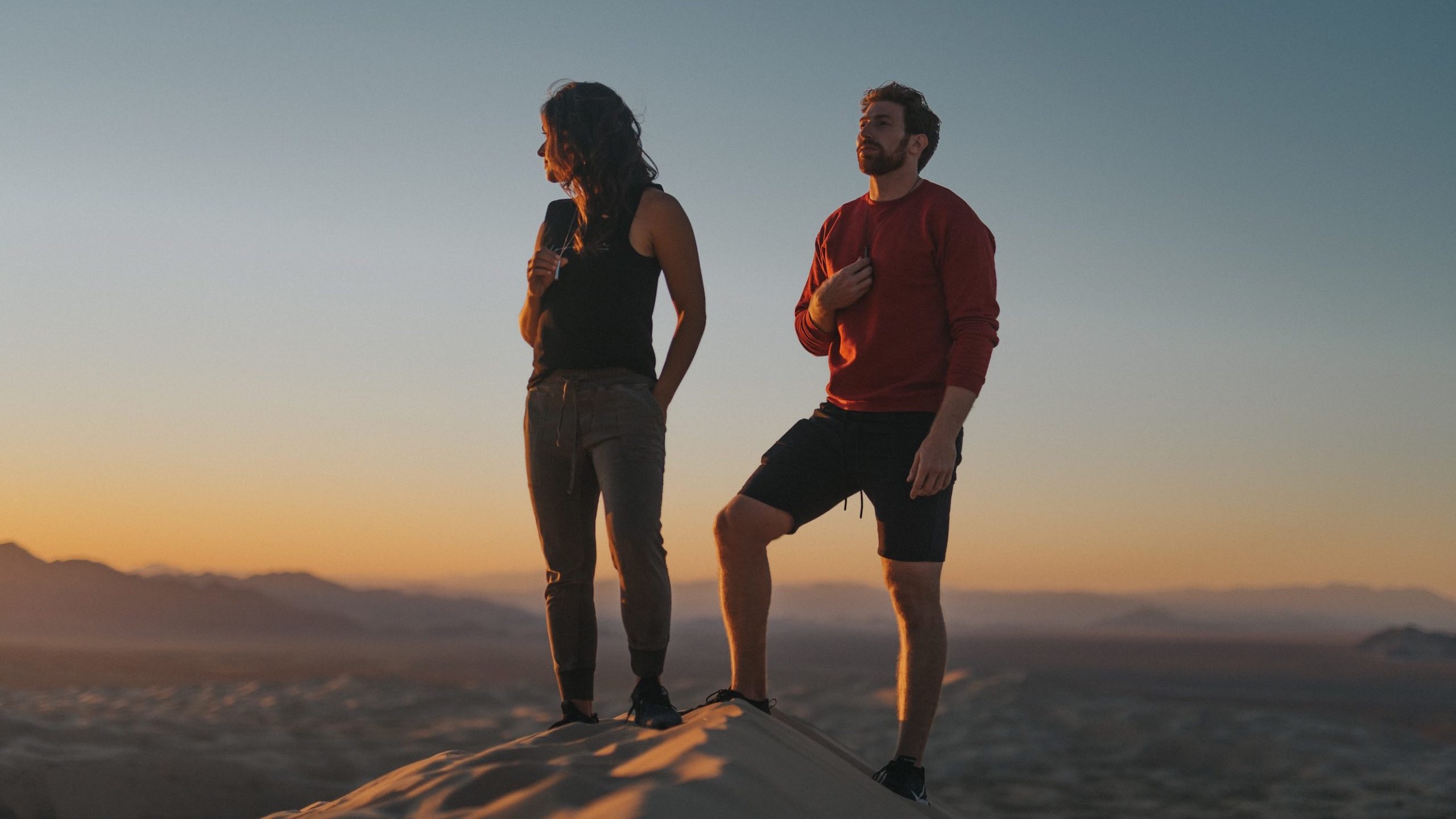 Komuso Video Production Los Angeles with man and woman standing on a sand mound at sunset with small hills in the background holding the whistle hanging around their necks