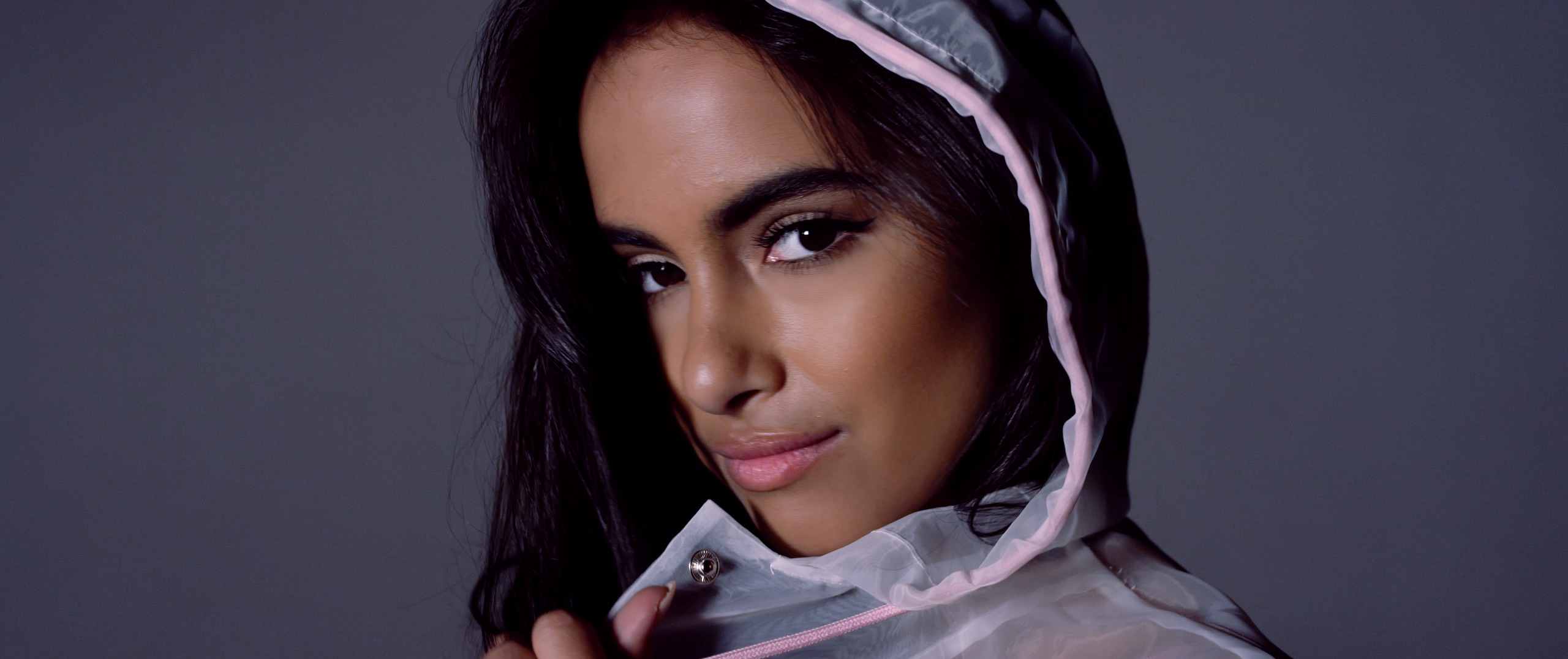 The Dailies Episode 202 BTS Footage with closeup headshot of Mercedes Gutierrez wearing a pink and white rain coat