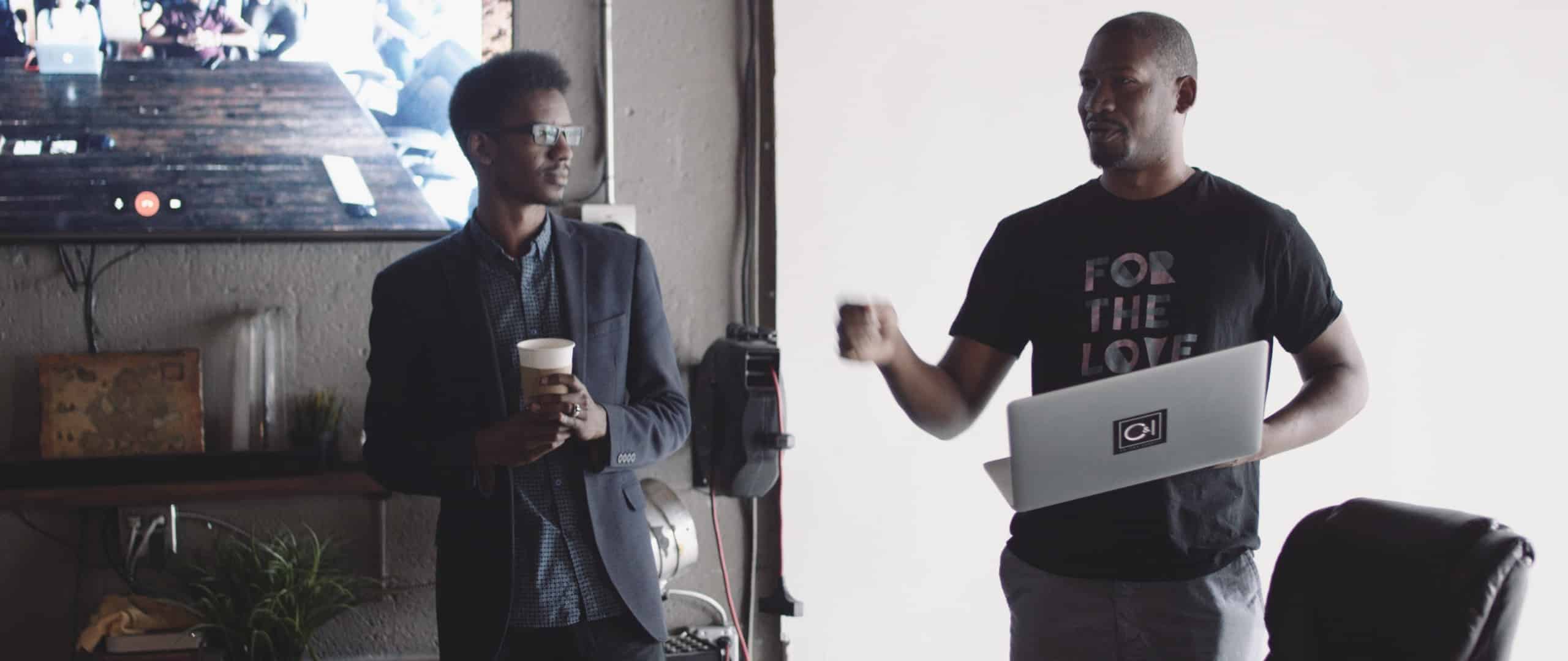 Video Production Sales Pitch with Joseph holding a laptop and Justin Miller holding a cup of coffee in an office