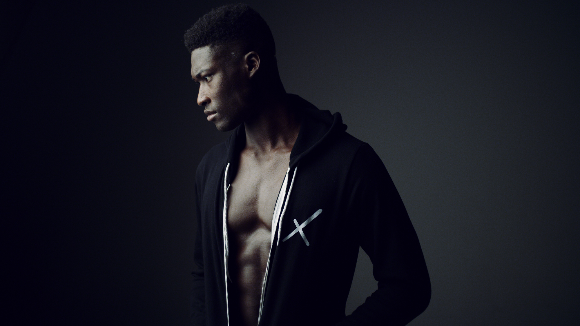 Uncreative Shop Side profile headshot of African American male model posing for camera wearing a black jacket with white Uncreative logo looking off camera