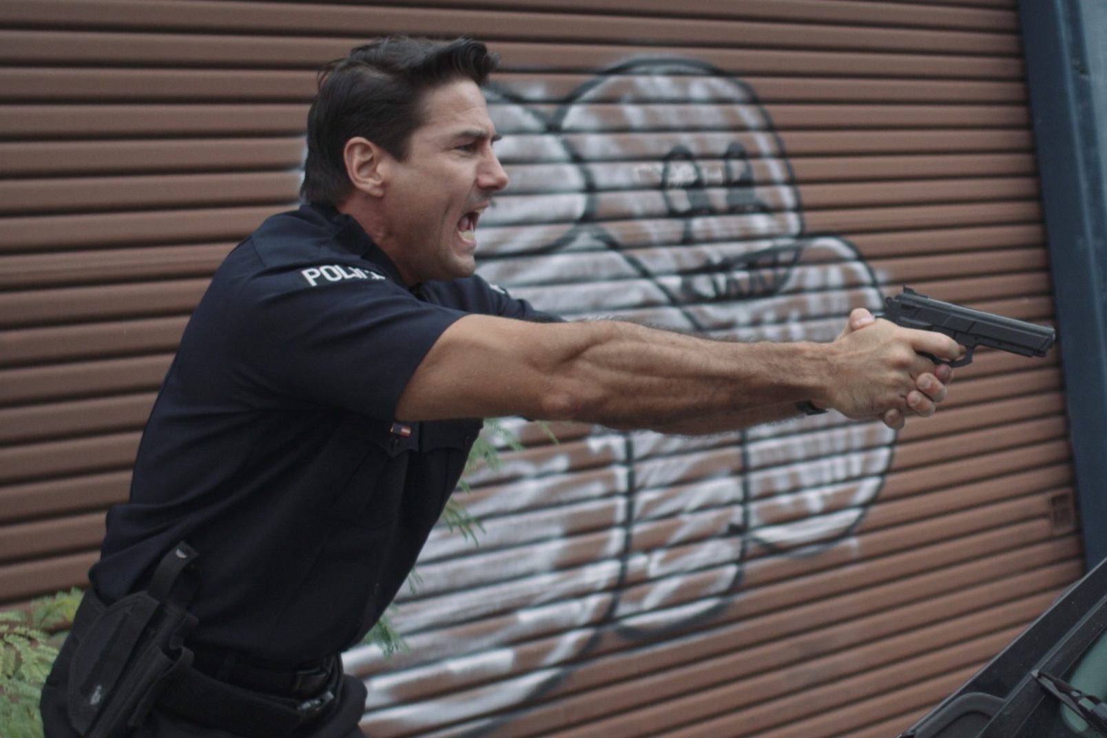 Production Resources Props Side profile of police officer wearing uniform holding a gun in outstretched hands shouting with graffiti on wall behind him