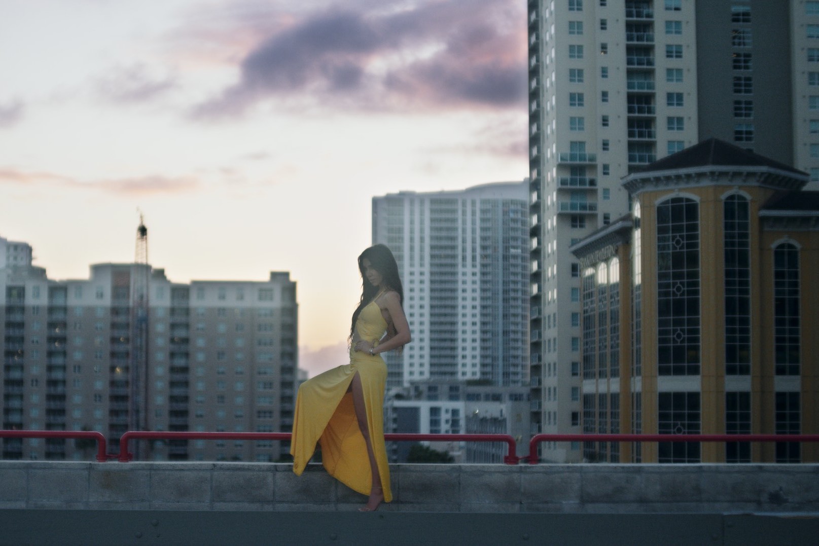 Production Resources South Florida Locations Side profile of woman wearing a yellow dress standing on a rooftop by a red railing in a city