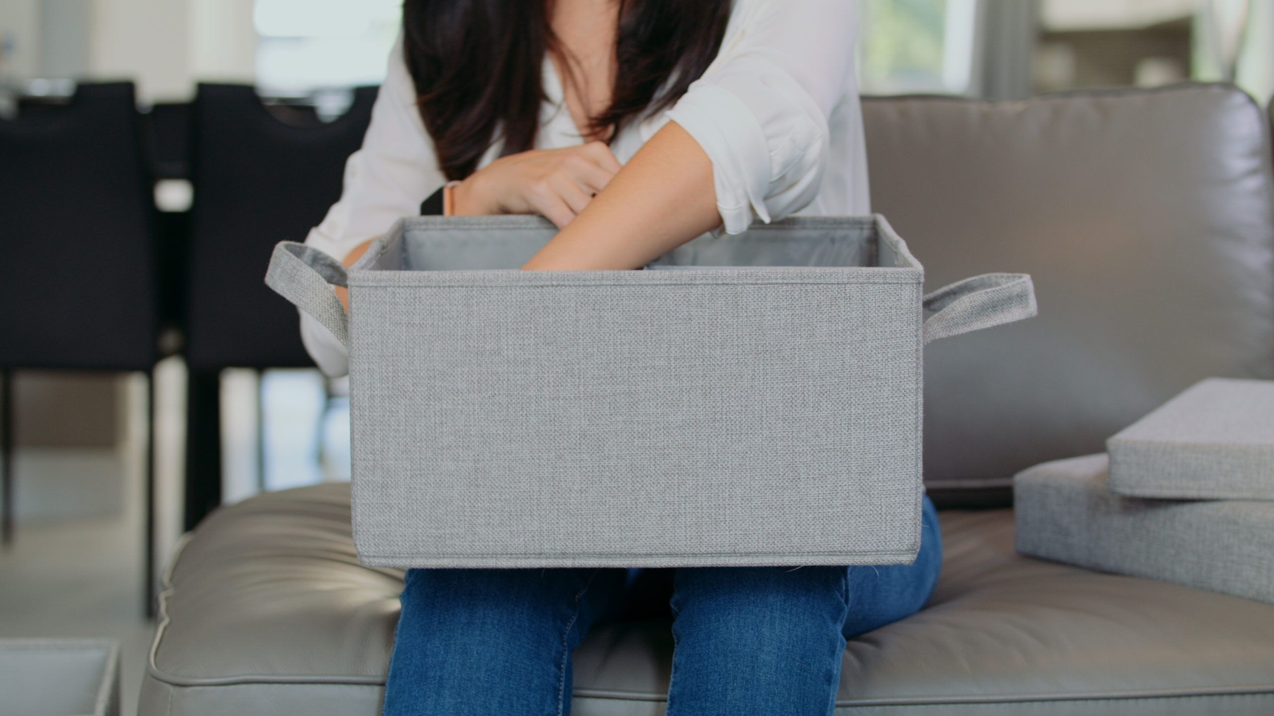 Audy Global Enterprise Ottoman Woman wearing jeans reaching into a box while sitting on a couch