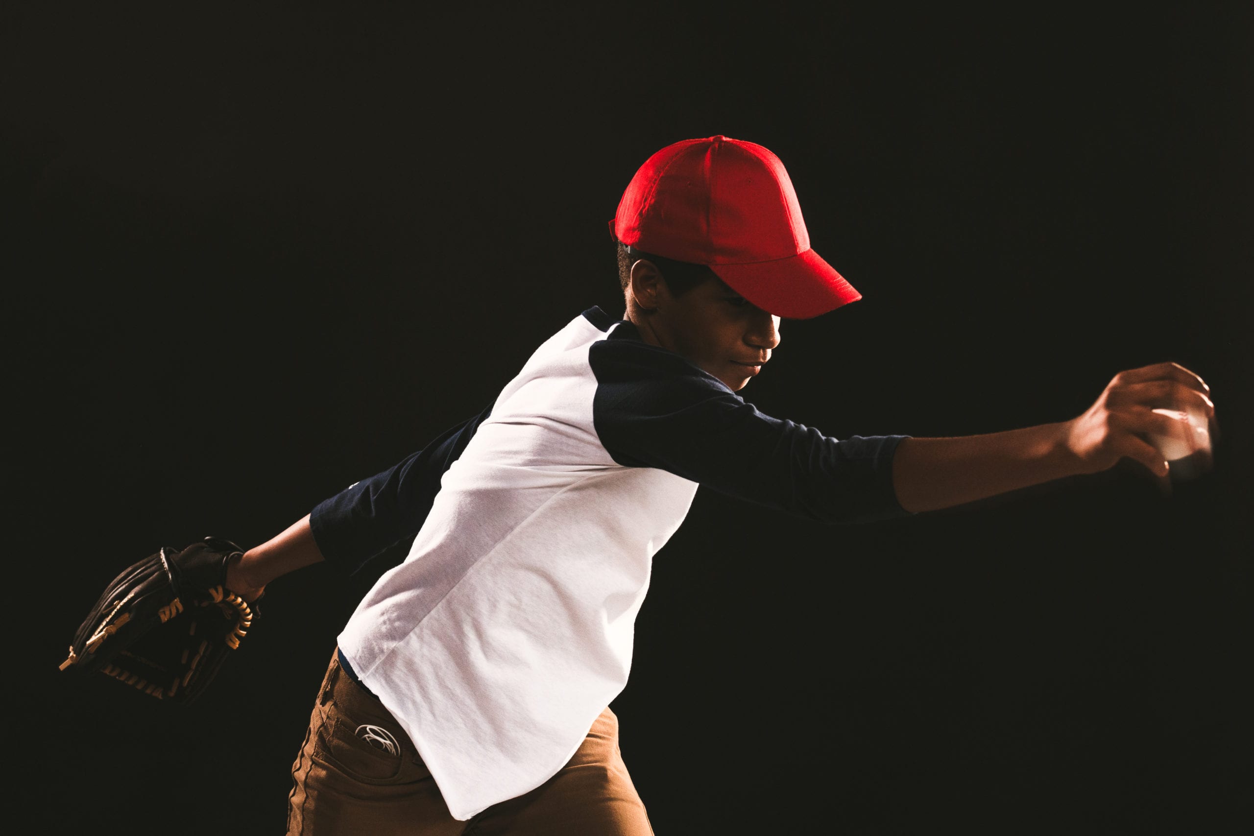 IU C&I Studios Ball Cap Liner Side profile of a young baseball player wearing a red cap in a pitching pose