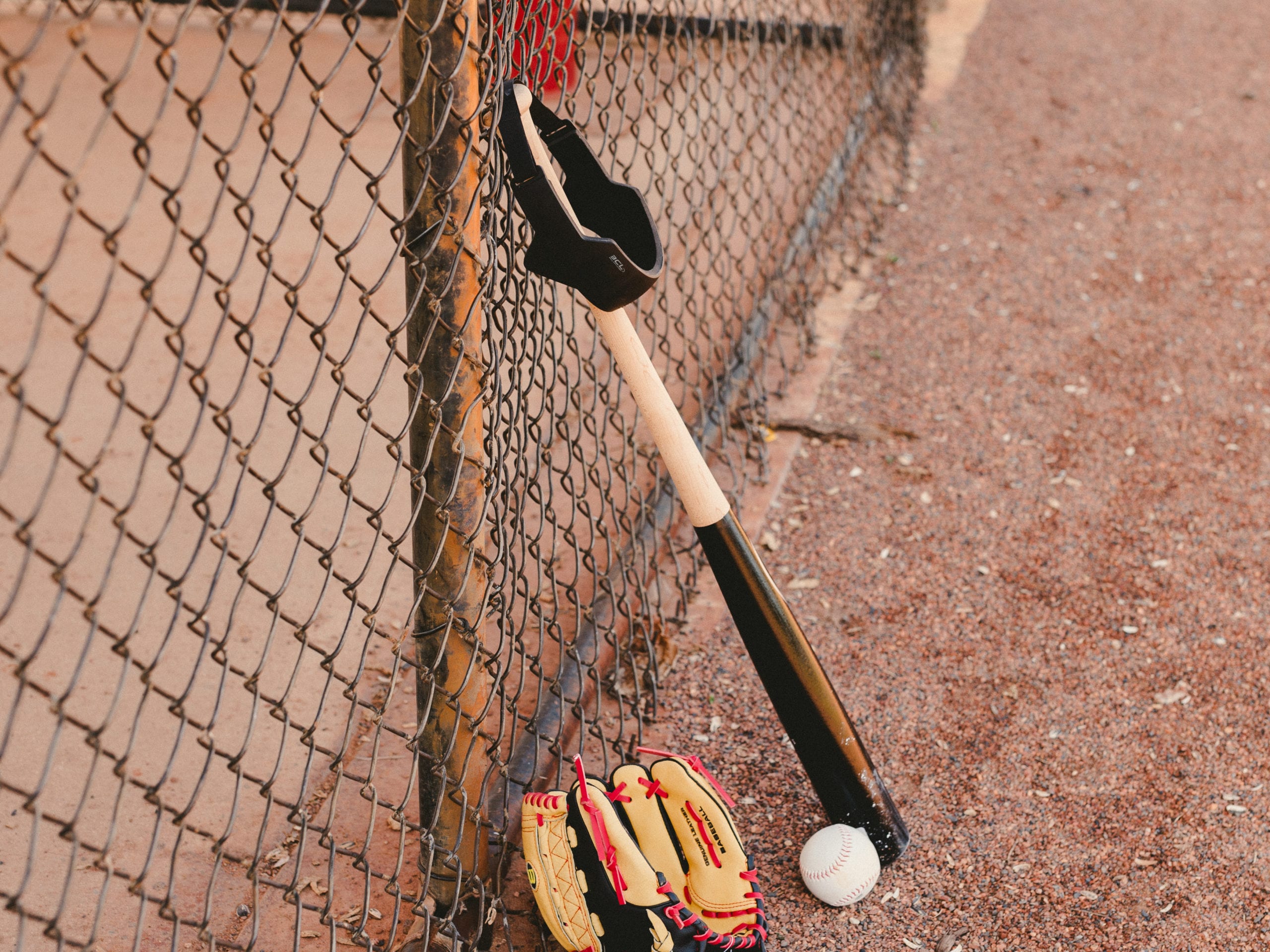 IU C&I Studios Portfolio Ball Cap Liner Closeup of baseball mitt and baseball on the ground and baseball bat leaning against a chain link fence with a BCL hanging on the bat