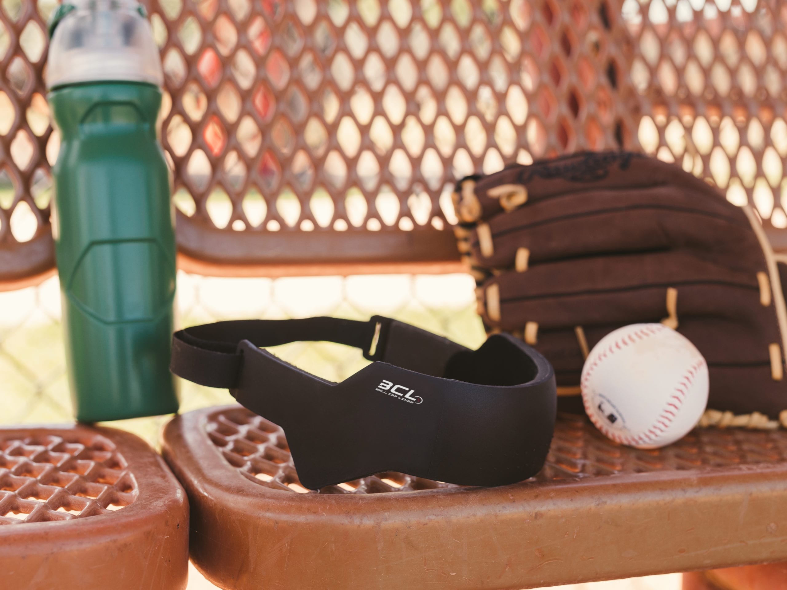 IU C&I Studios Ball Cap Liner Closeup of water bottle, BCL, baseball and mitt resting on baseball field bench