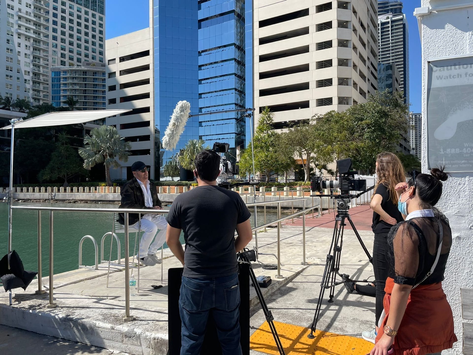 View from behind of staff filming a man sitting on a chair by the water