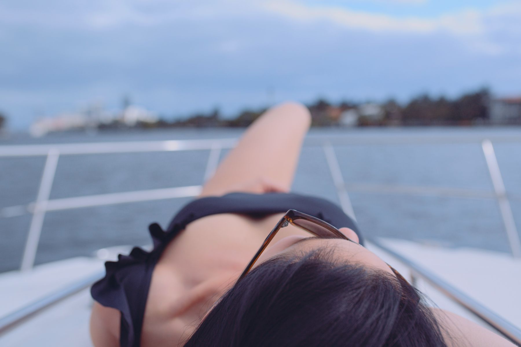 IU C&I Studios Portfolio Macken Koya Bay Closeup of a woman wearing a black bathing suit and sunglasses sunbathing on a white yacht