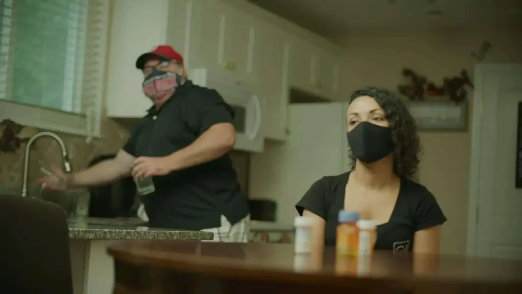 Staff 7 Ciara Santiago seated at a table wearing black mask with man next to her also wearing a mask using kitchen sink