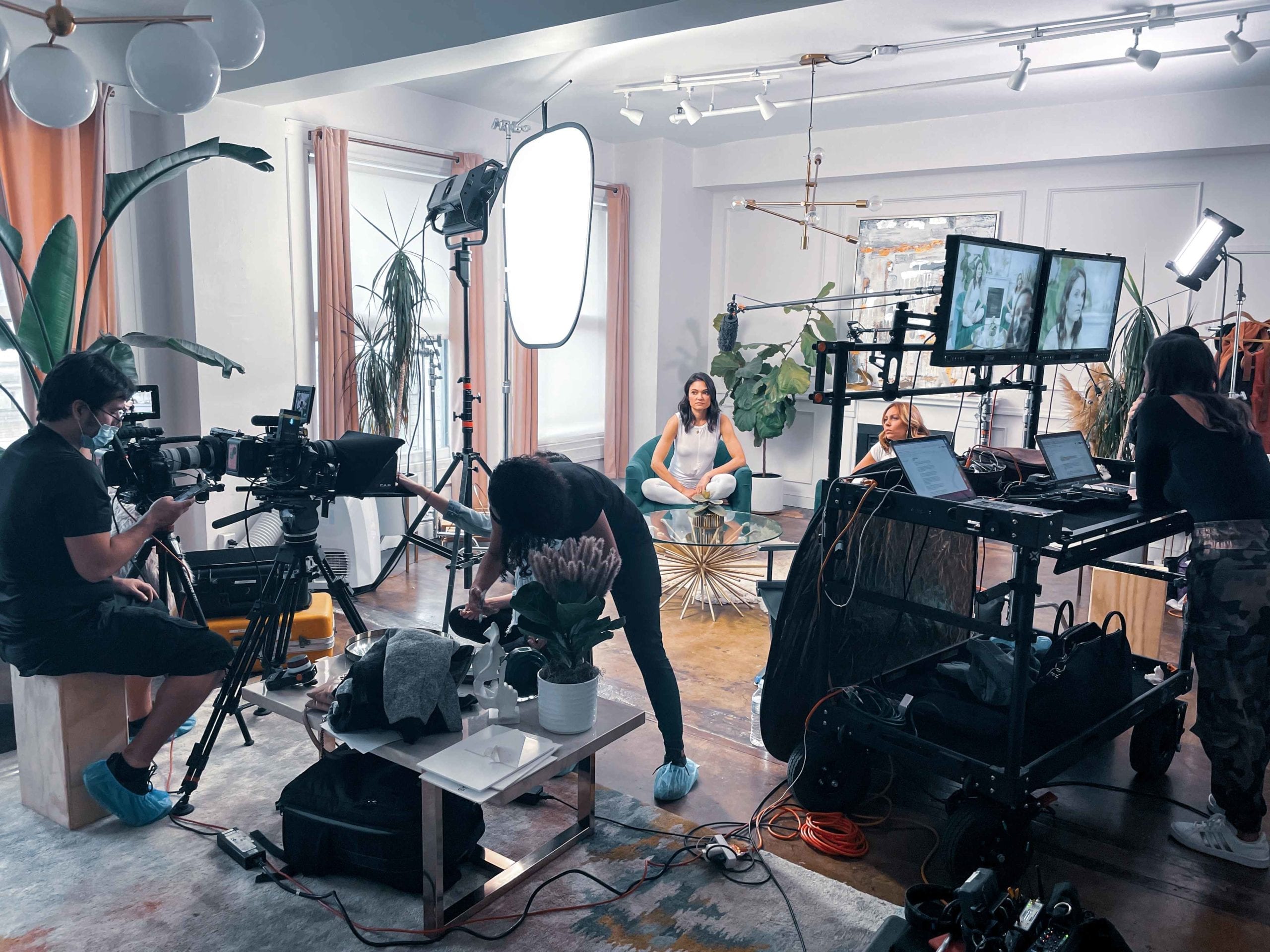 Woman sitting in a teal colored chair surrounded by camera and computer crew