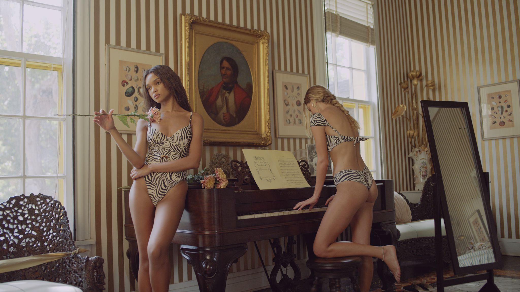 IU C&I Studios Portfolio Two female models wearing black and white swim suits in a room with one holding a flower leaning against the piano and the other playing the piano