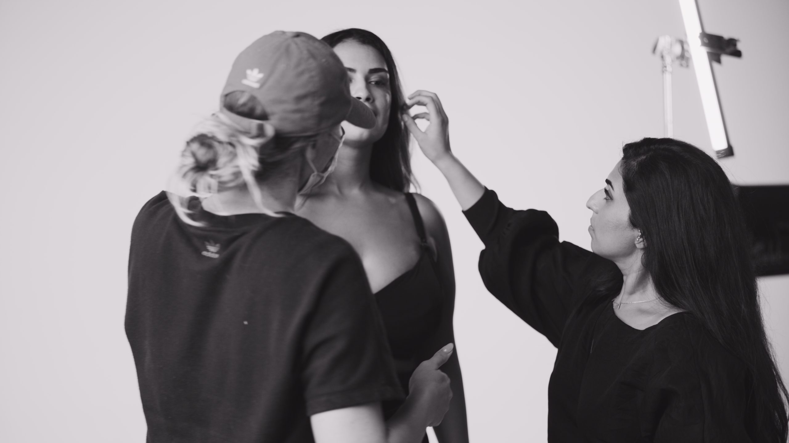 Black and white of two women helping with makeup on model wearing bra