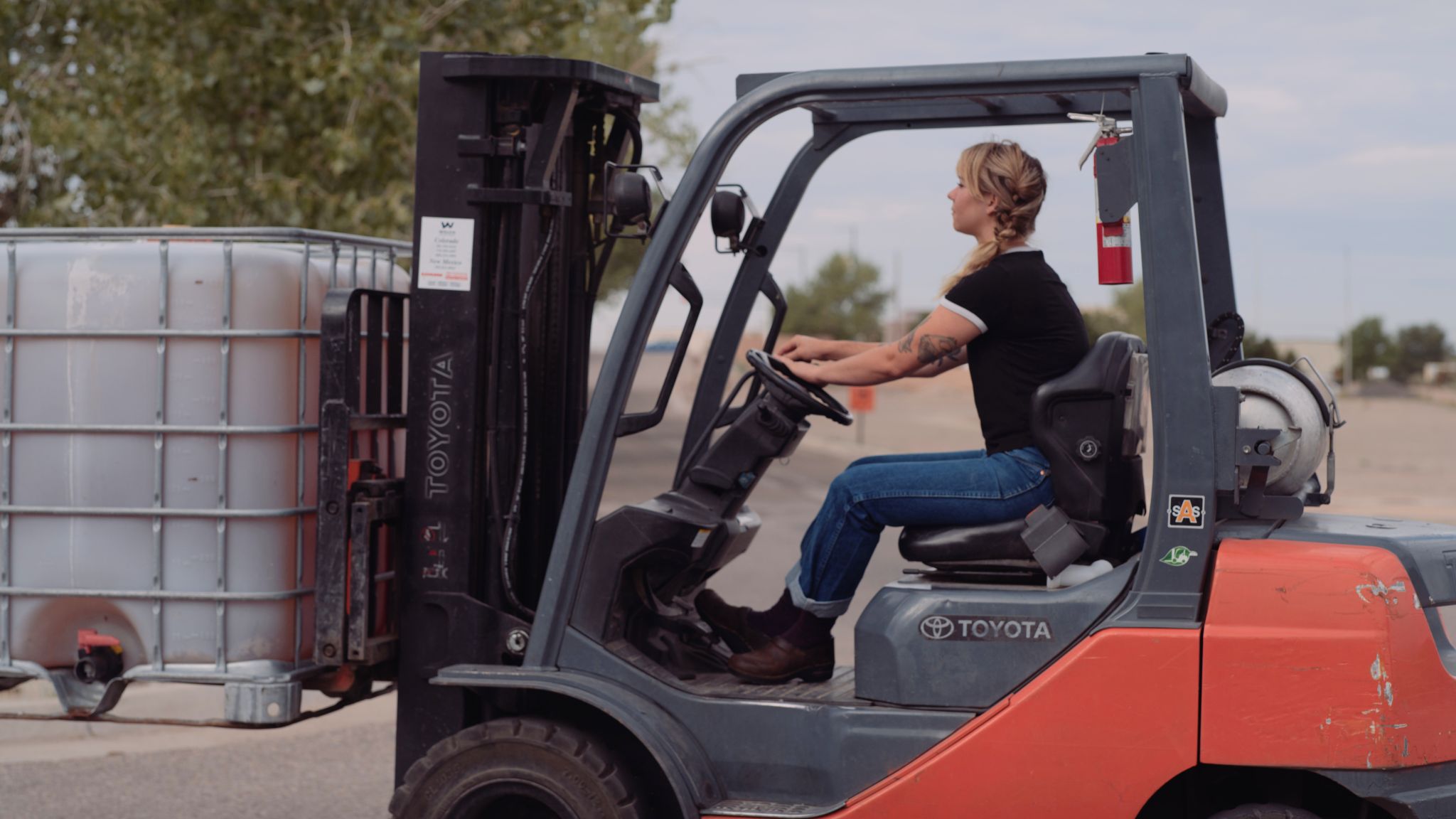 IU C&I Studios Portfolio Taylor Garrett Spirits Side profile of tattooed long blond haired woman wearing jeans and black and gray t shirt using a forklift