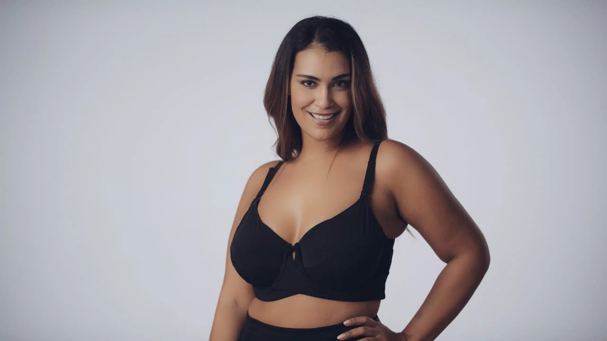 Model with long brown hair posing and smiling wearing the black bra