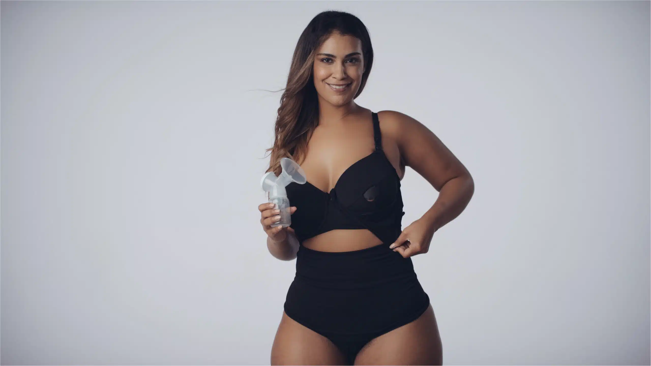 Model with long brown hair posing wearing the black bra and panties and holding a breast pump