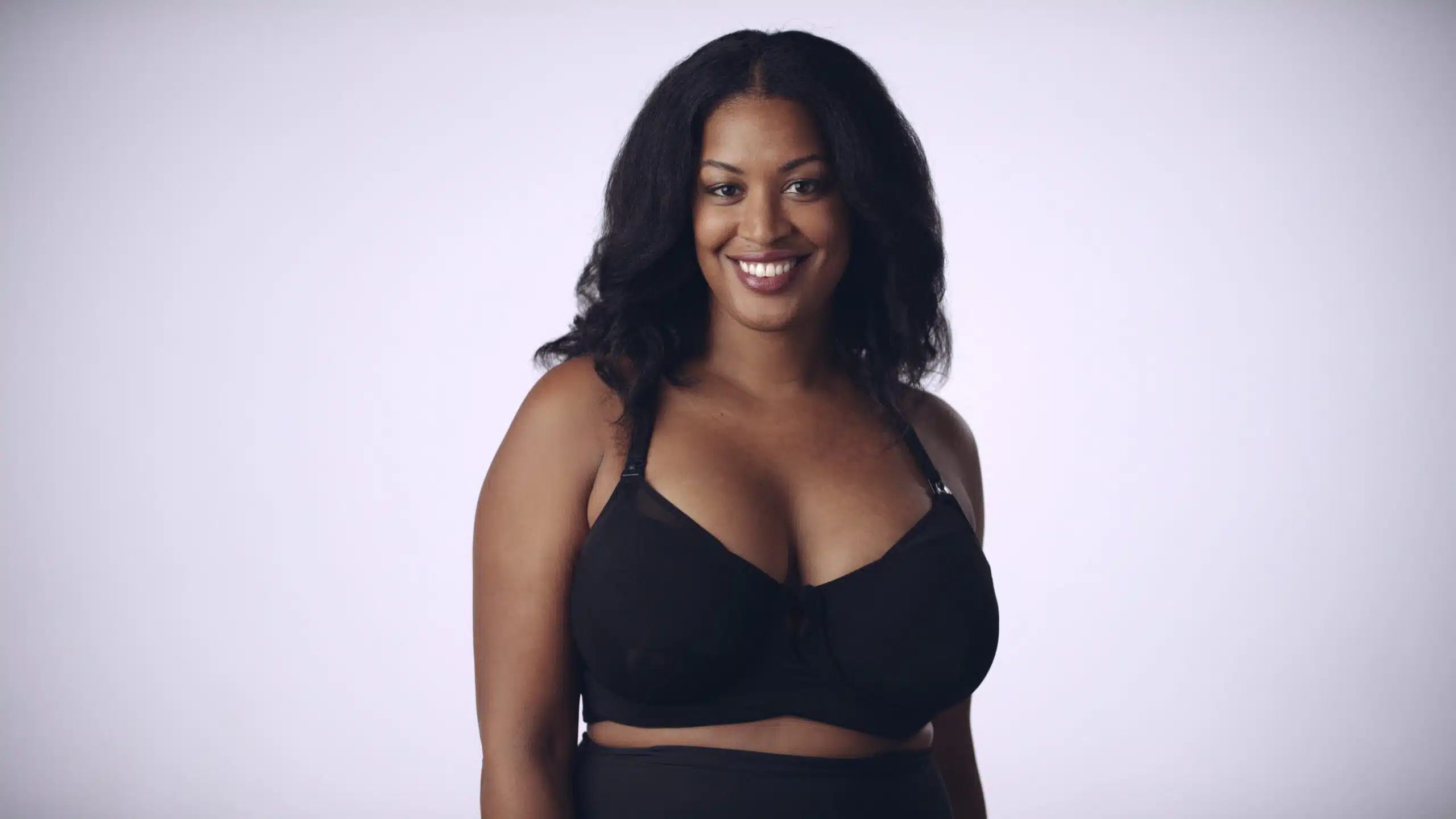 Model with fizzy brown hair posing and smiling for the camera wearing the black bra