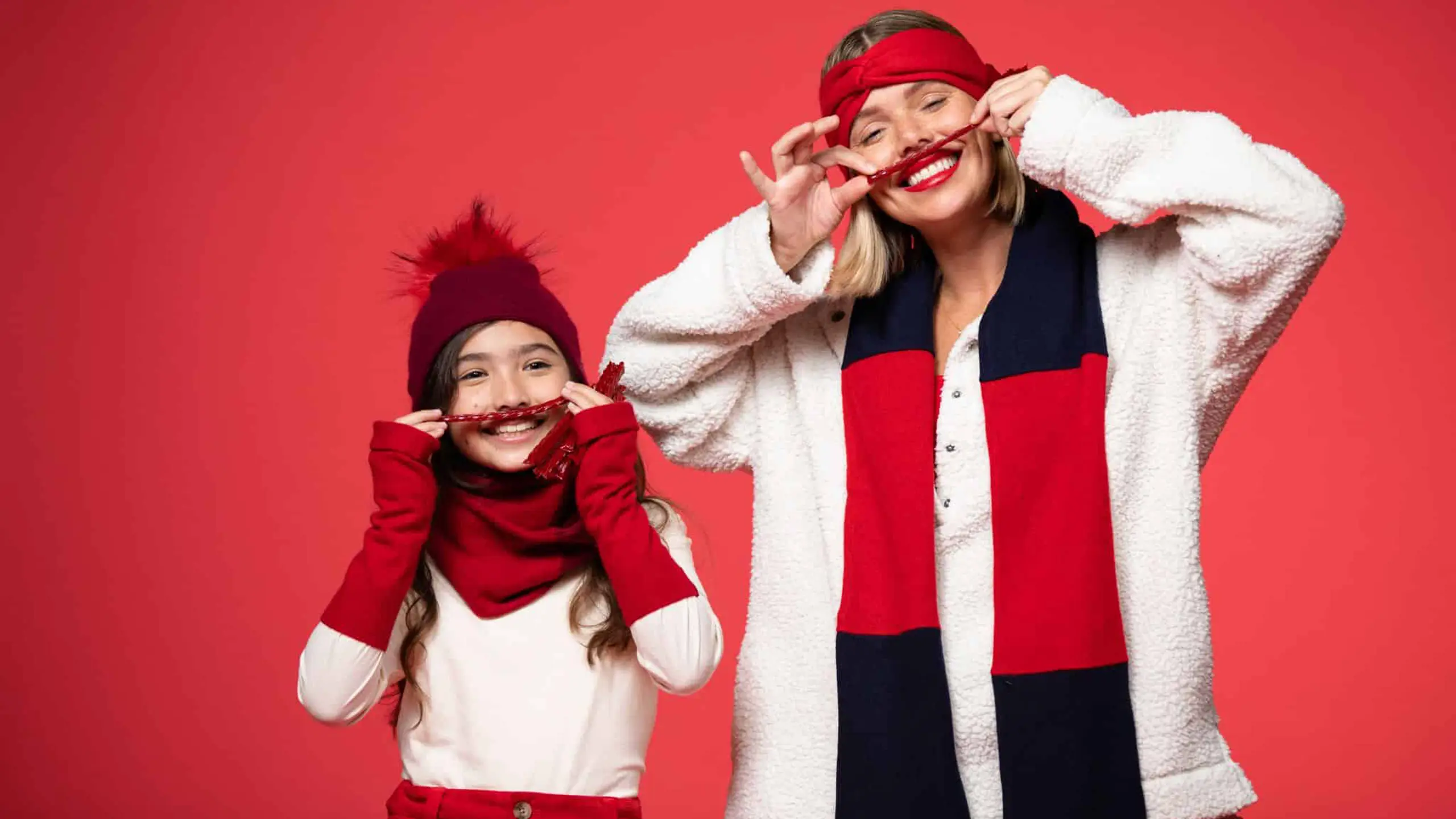Girl model wearing red headband, scarf and pants along with white top and female model wearing red hand band, white jacket and black and red scarf against a red backdrop