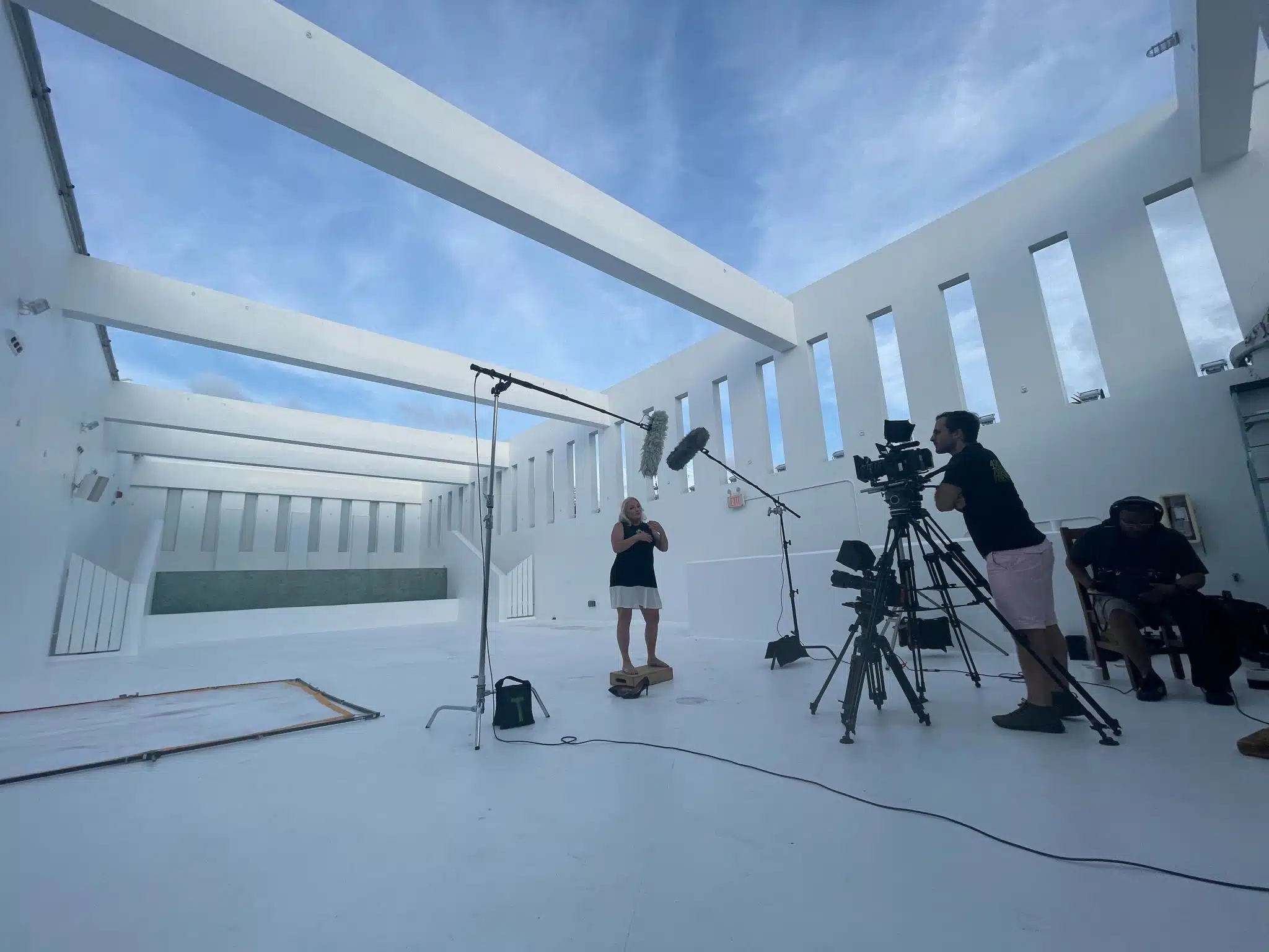 Crew filming woman wearing a white skirt and black top talking on a set