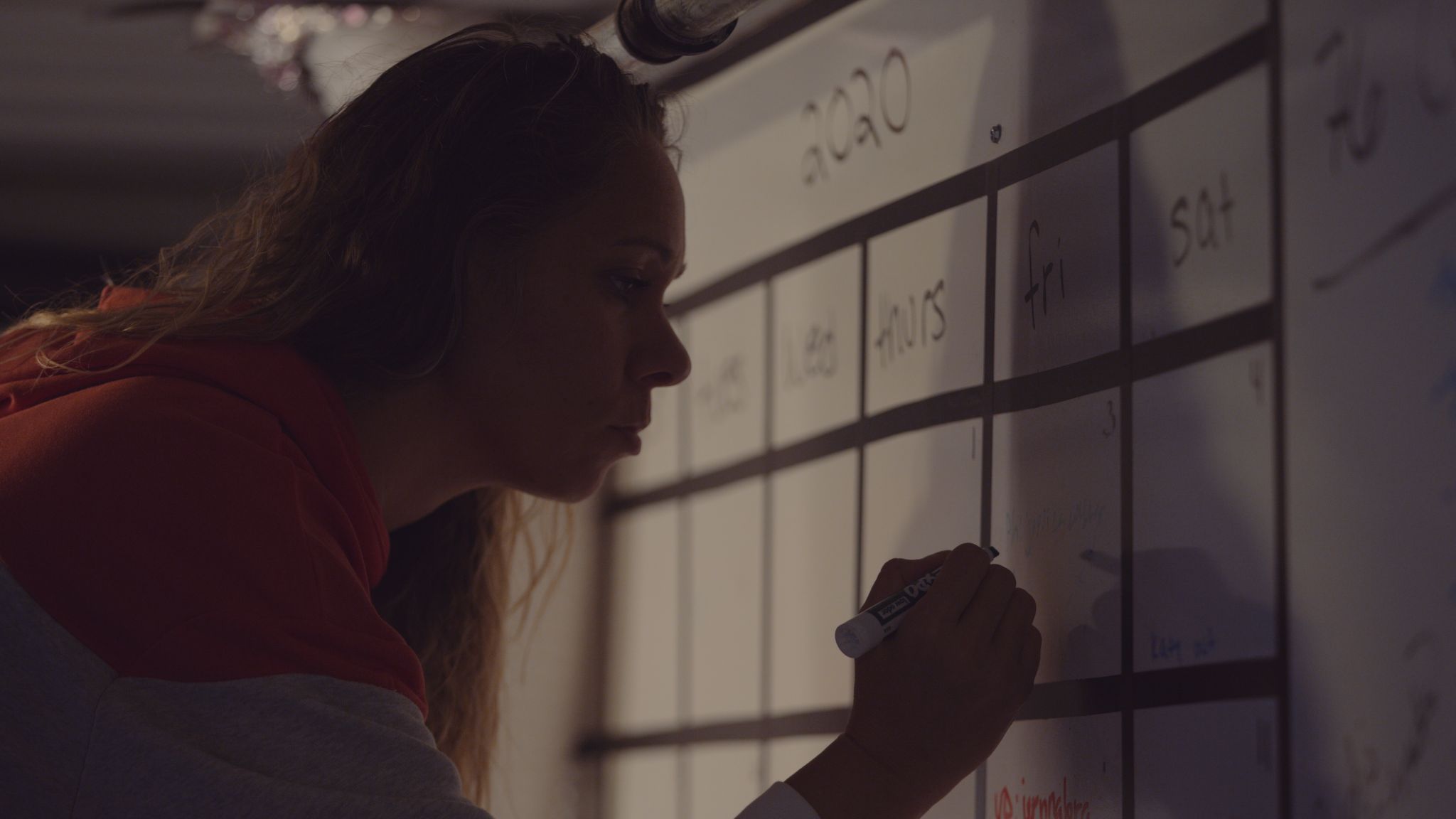 Side profile of woman writing something in a calendar on a white board