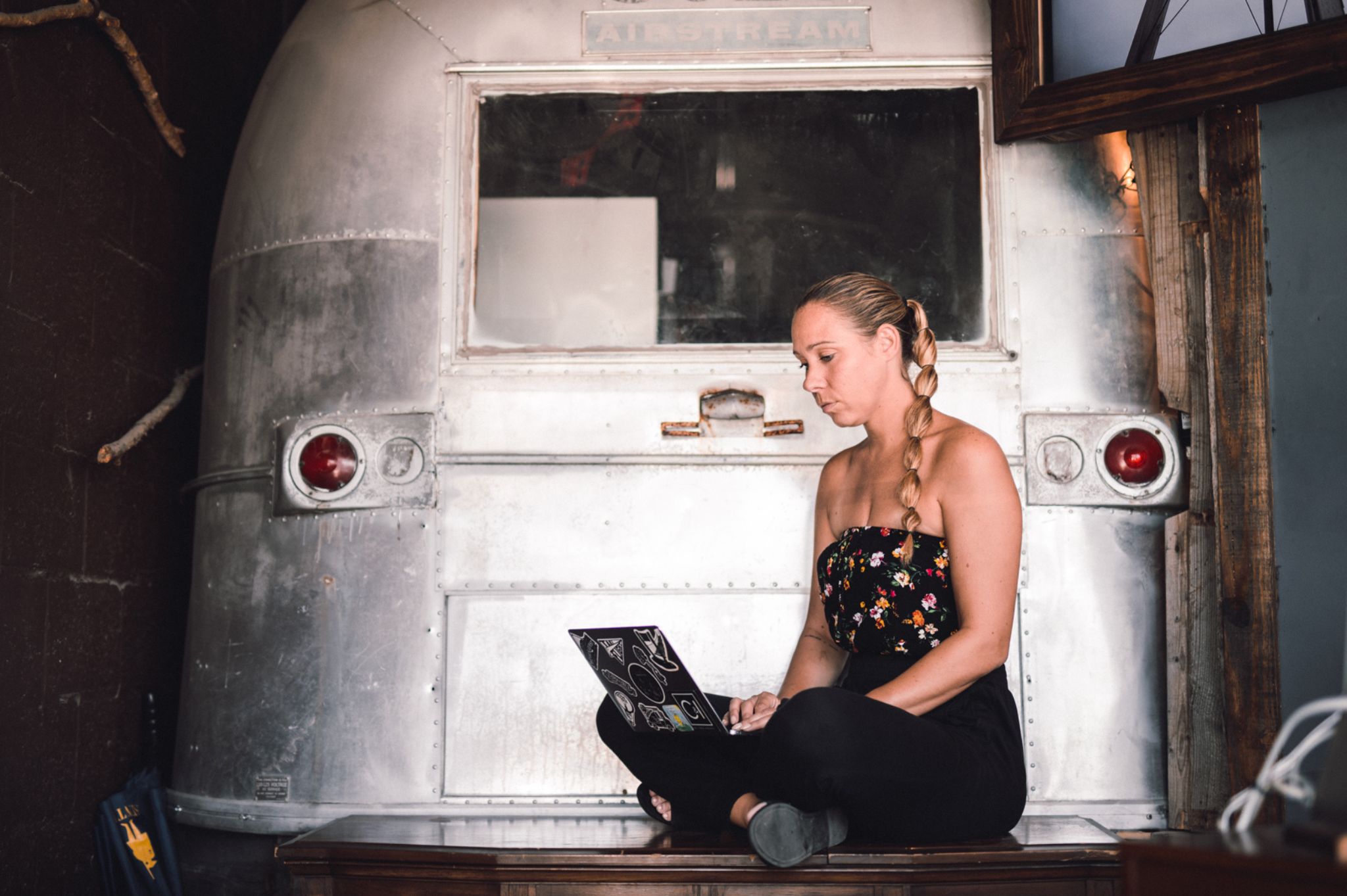 Ways to spot good filming locations Side profile of woman with long hair in a braided ponytail working on a laptop sitting behind an old metallic RV