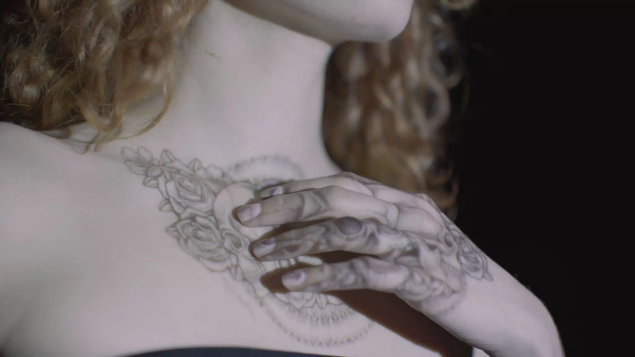 Closeup of woman with blond curly hair having tattoo image displayed on her chest