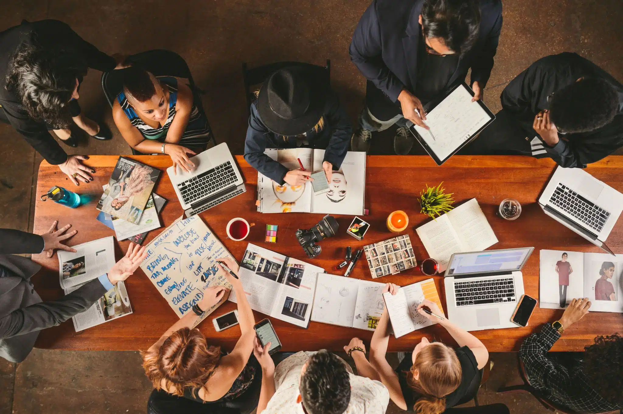 The difference between a freelancer and creative agency Industry Showdown Freelancer vs Creative Agency Overhead view of people at a table having a discussion with laptops and notebooks