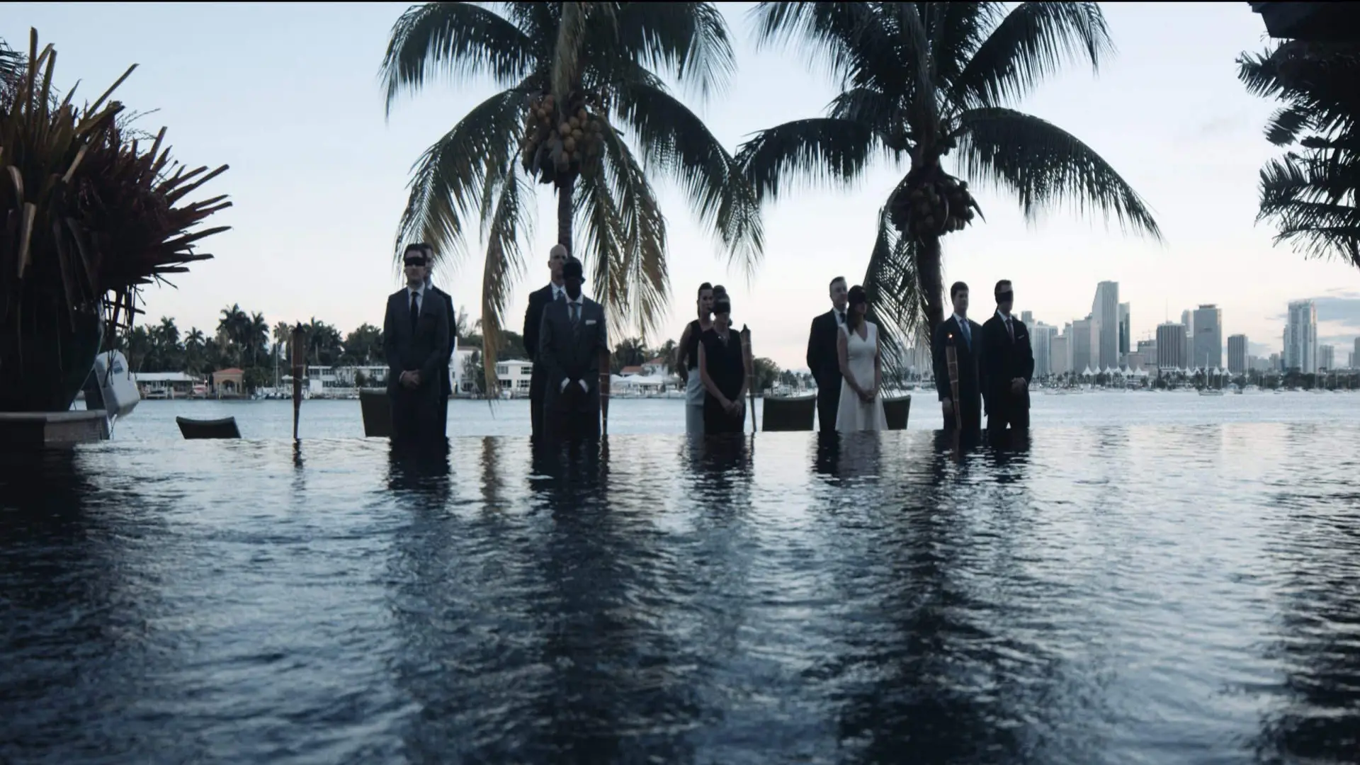 Five couples standing near water with palm trees and city behind them