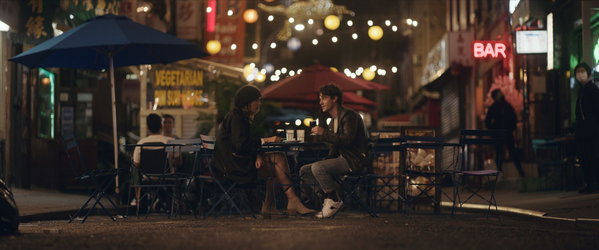 A couple sitting at a table and enjoying drink talking on a restaurant patio in the city at night.