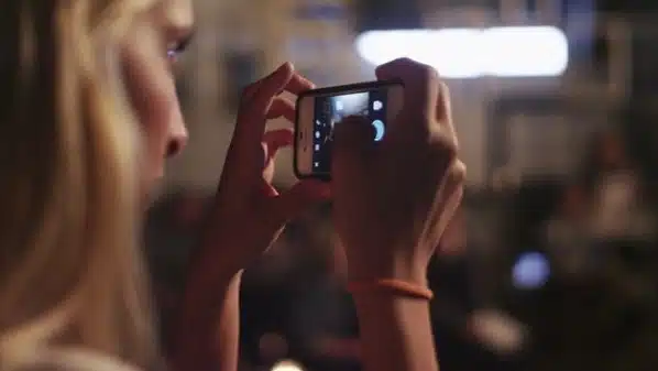 Side profile of woman with long blond hair taking a picture with cell phone