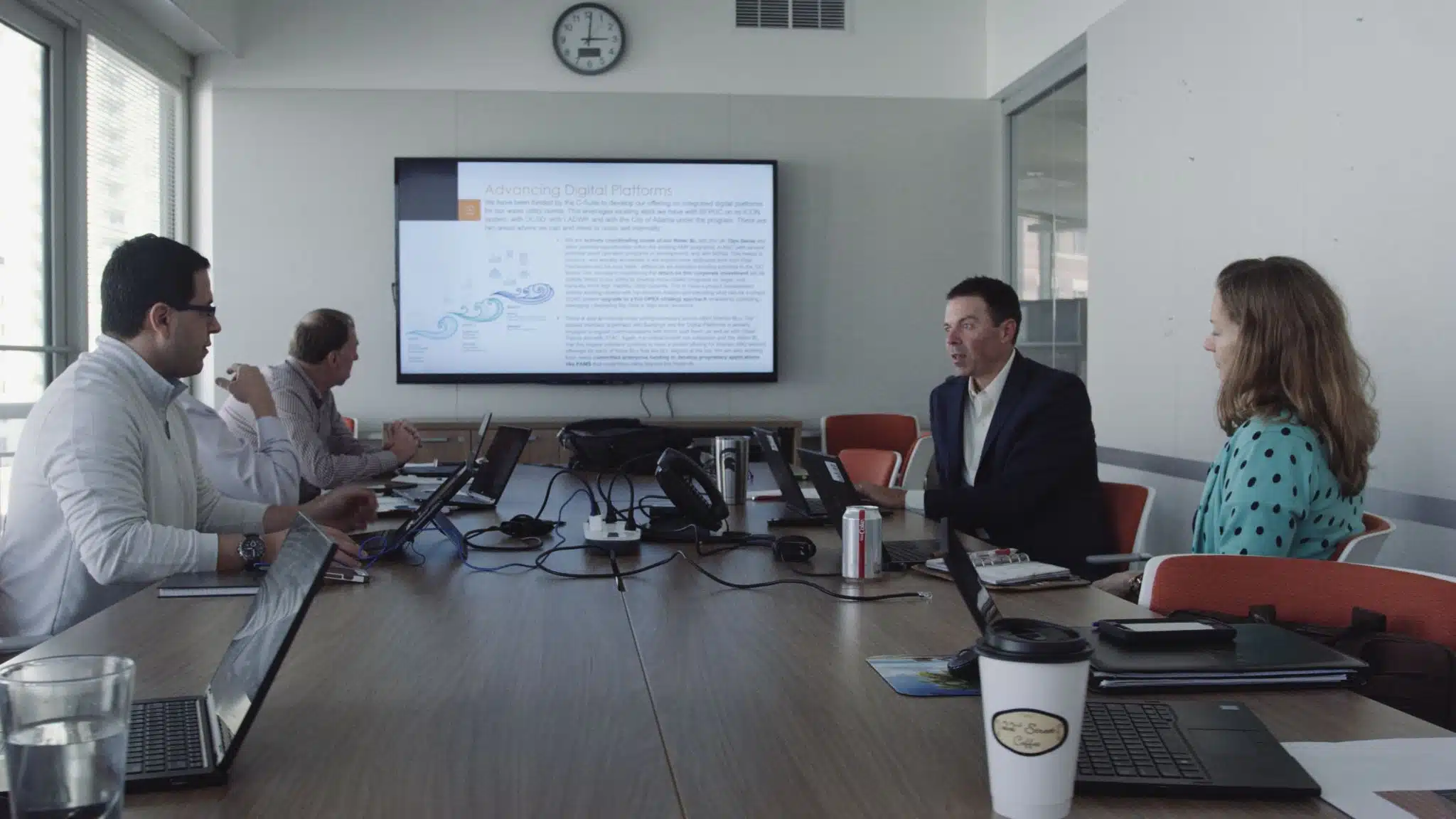 Three men and a woman in a conference room going over stuff with laptops